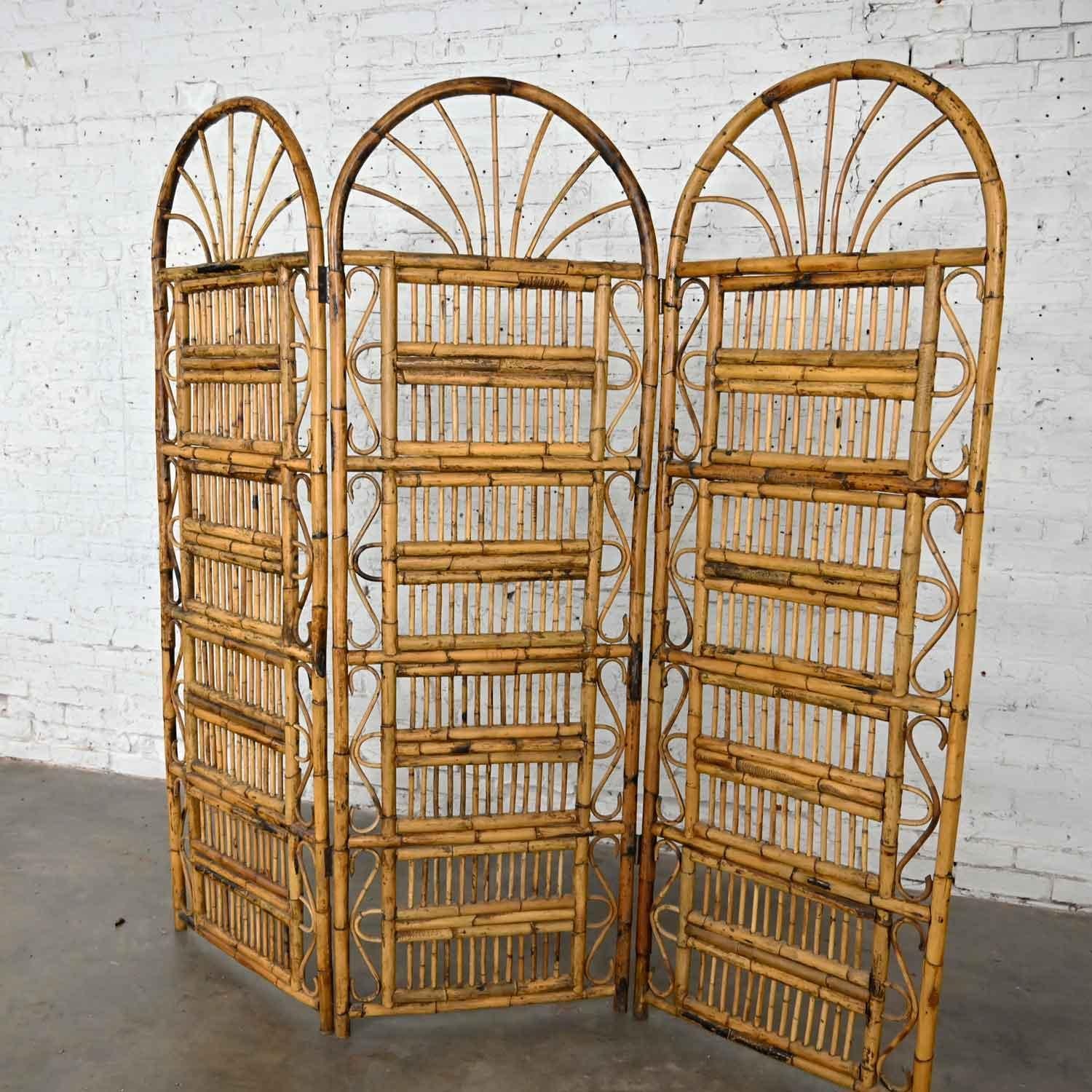 Gorgeous vintage Hollywood Regency & Organic Modern rattan three panel folding screen with arched tops, brass plated hinges, and serpentine loop details on the edges. Beautiful condition, keeping in mind that this is vintage and not new so will have