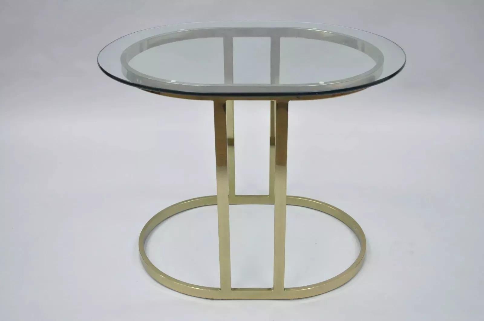 Table d'appoint ovale en métal plaqué laiton et verre Vintage Hollywood Regency. L'objet présente des lignes modernes et épurées, un plateau ovale en verre et une base ovale en métal plaqué laiton. Circa Late 20th Century. Dimensions : 21,5
