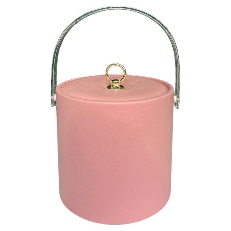 A Hollywood Regency or Palm Beach Regency style pink ice bucket with acrylic handle. This will be a fabulous addition to your bar at your next cocktail party. It is round, and covered in pink textured vinyl. (The fabric resembles leather, but is