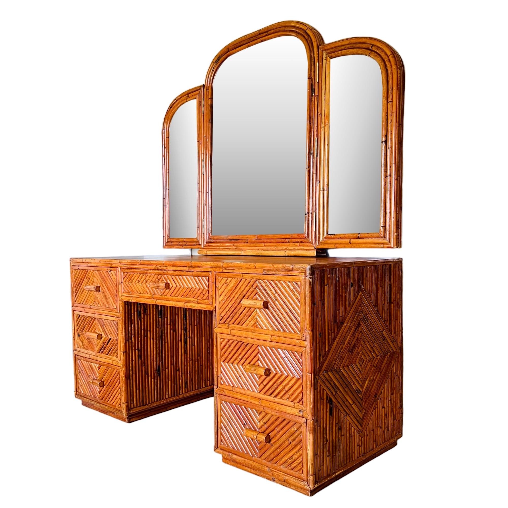 A vintage Palm Beach Regency split reed rattan dressing table or desk with mirror. This large vanity features seven spacious drawers, a solid teak wood top surface, diamond pattern detail extending through the drawer faces and on the side panels,