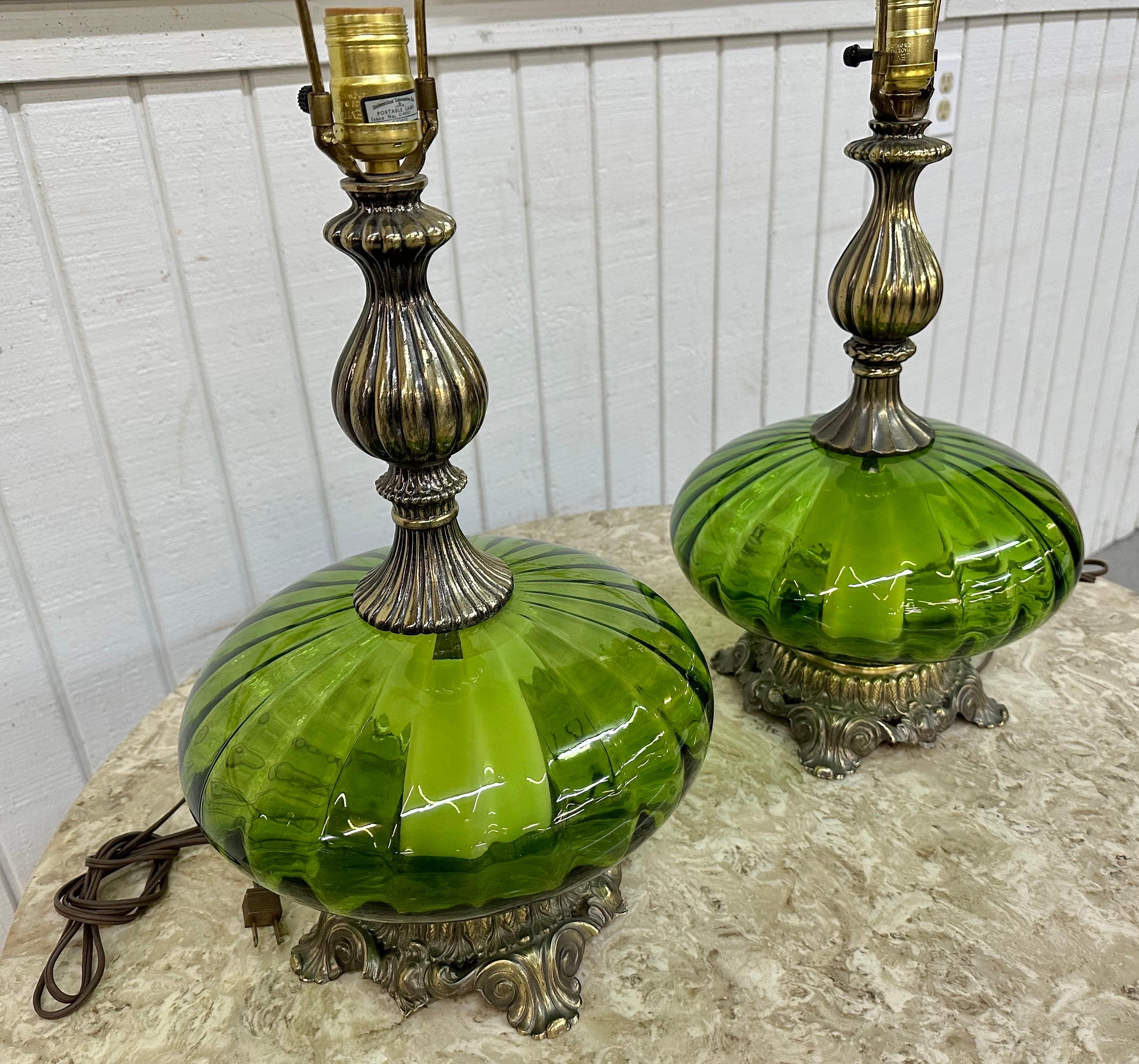 This listing is for a pair of vintage Hollywood Regency Style Green Glass Table Lamps. Featuring a brass base, a green glass body, and original harps and cords. This is an exceptional combination of quality and design!