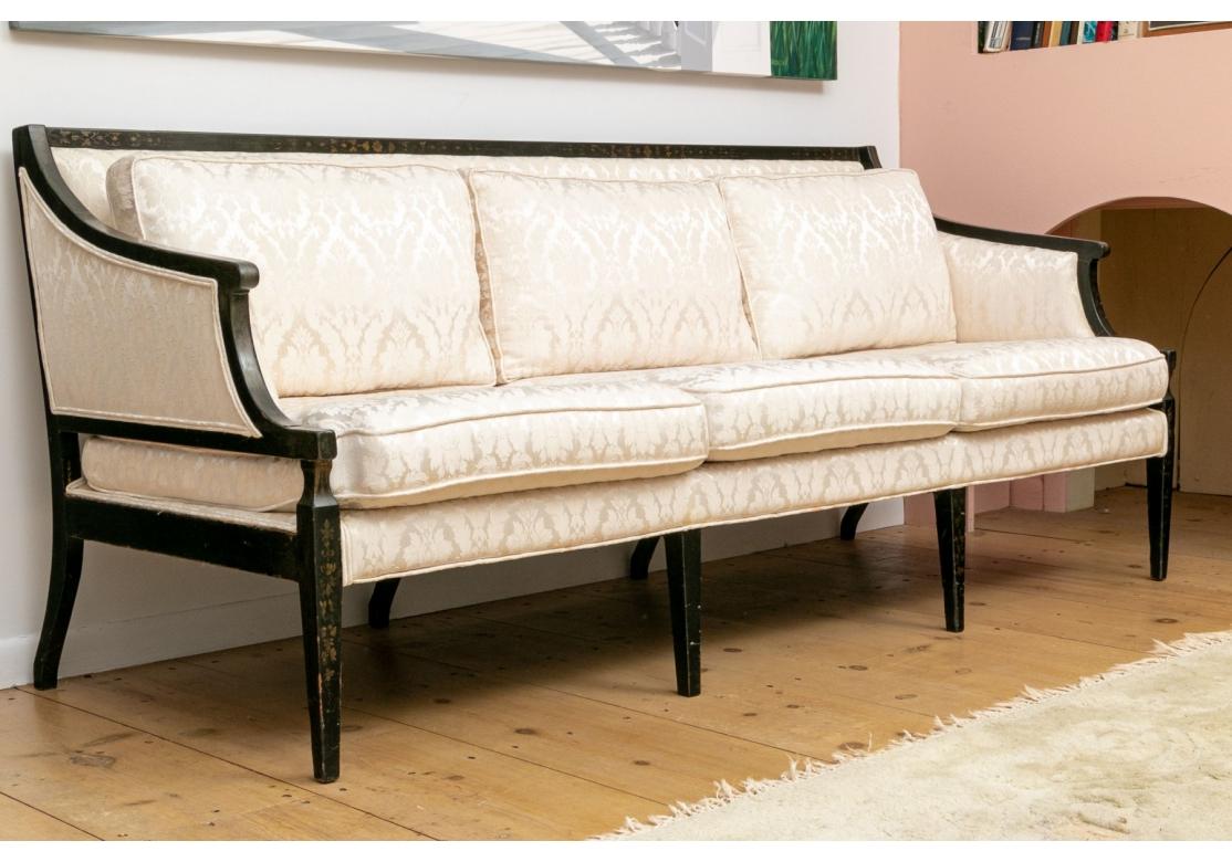 Vintage Hollywood Regency style sofa with loose seat cushions and back cushions on a tight back. The ebonized frame with sloop arms, gold stenciled front legs and splayed back legs. The sofa is covered in a neutral jacquard fabric and hard to tell