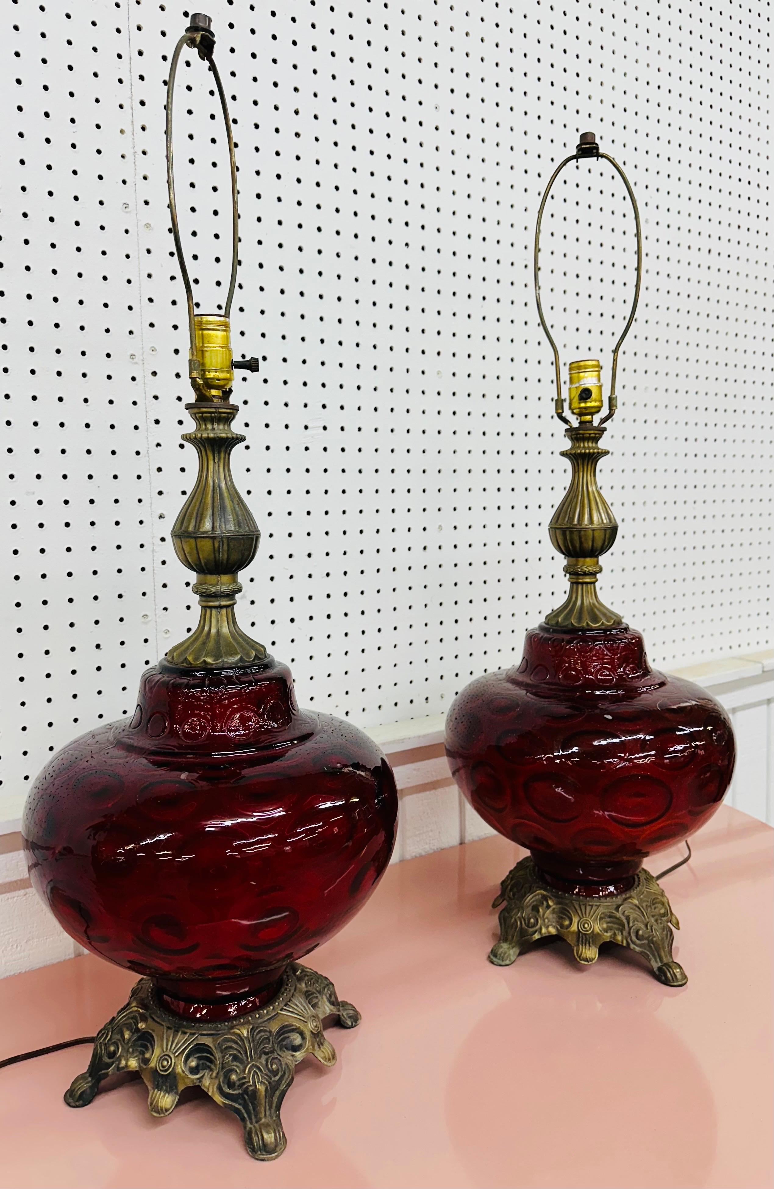 This listing is for a pair of vintage Hollywood Regency Style Ruby Red Glass Table Lamps. Featuring a brass base, a ruby red glass body, and original harp and cord. This is an exceptional combination of quality and design!