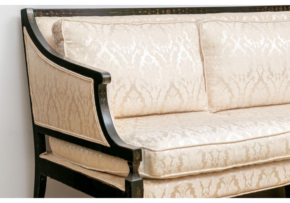 Vintage Hollywood Regency style sofa with loose seat cushions and back cushions on a tight back. The ebonized frame with sloop arms, gold stenciled front legs and splayed back legs. The sofa is covered in a neutral jacquard fabric and hard to tell