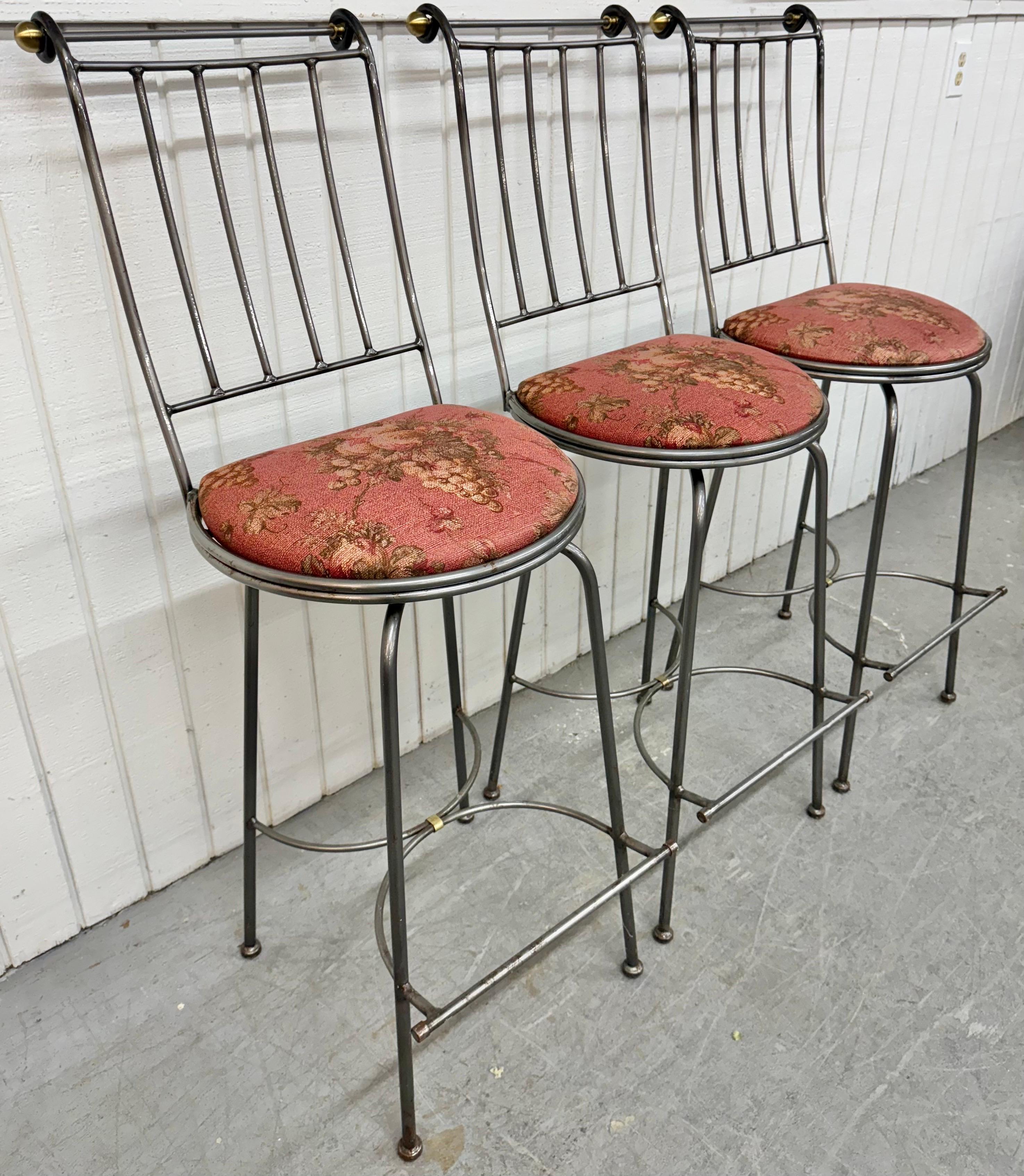 Questo annuncio si riferisce a un set di tre sgabelli da bar girevoli Vintage Hollywood Regency. Presenta una struttura in ferro, un supporto per lo schienale, una seduta imbottita, un poggiapiedi e un meccanismo girevole. Si tratta di una