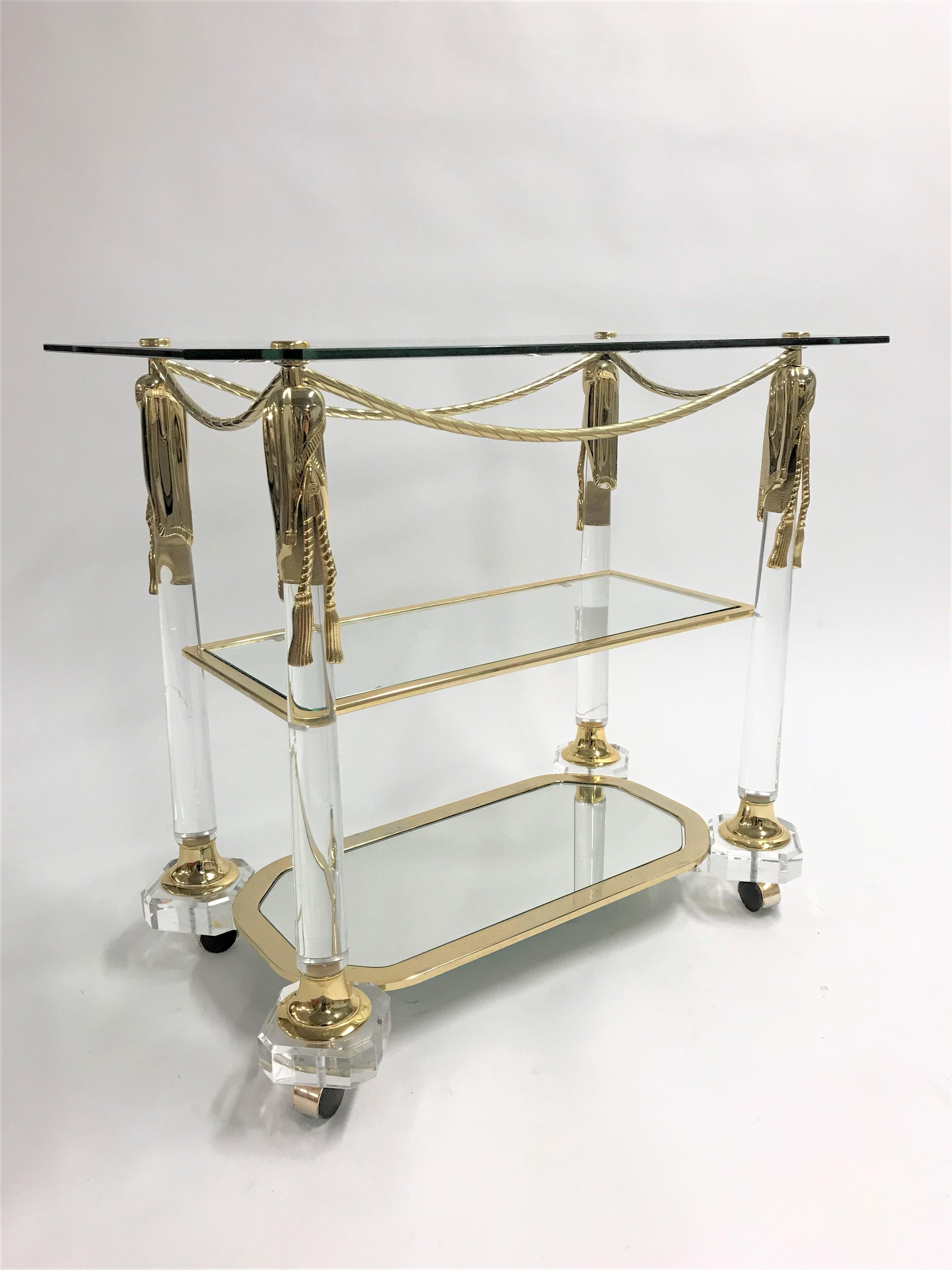 Vintage Hollywood Regency bar or serving trolley made from brass, Lucite and glass.

The trolley has Empire style decorations and shows some beautiful patina.

It features a mirrored glass shelve at the bottom and a cut glass top.

Beautiful