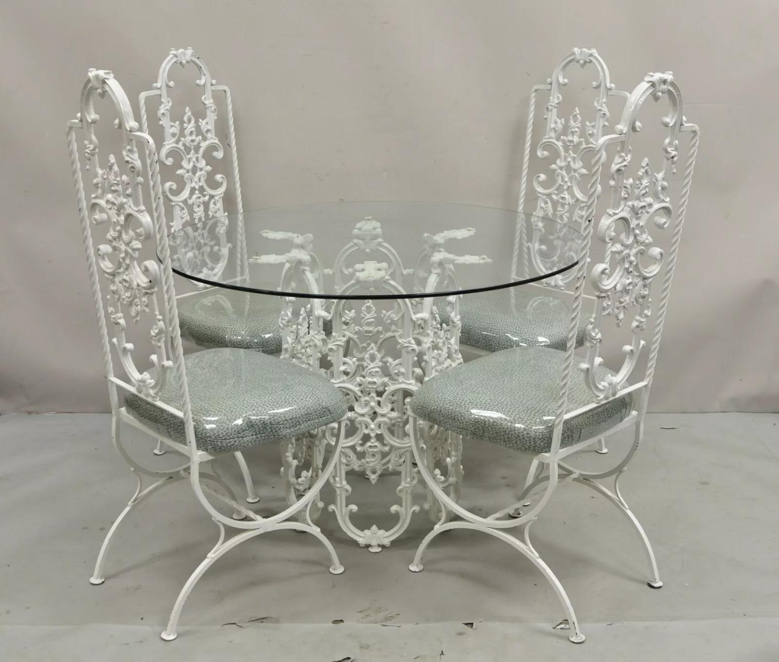Vintage Hollywood Regency White Ornate Wrought Iron Scrolling Dining Set - 5 Pc Set. Listing includes 4 high back wrought iron dining chairs and (1) round glass top pedestal base dining table. Circa Mid 20th Century. Measurements: Table: 29.5