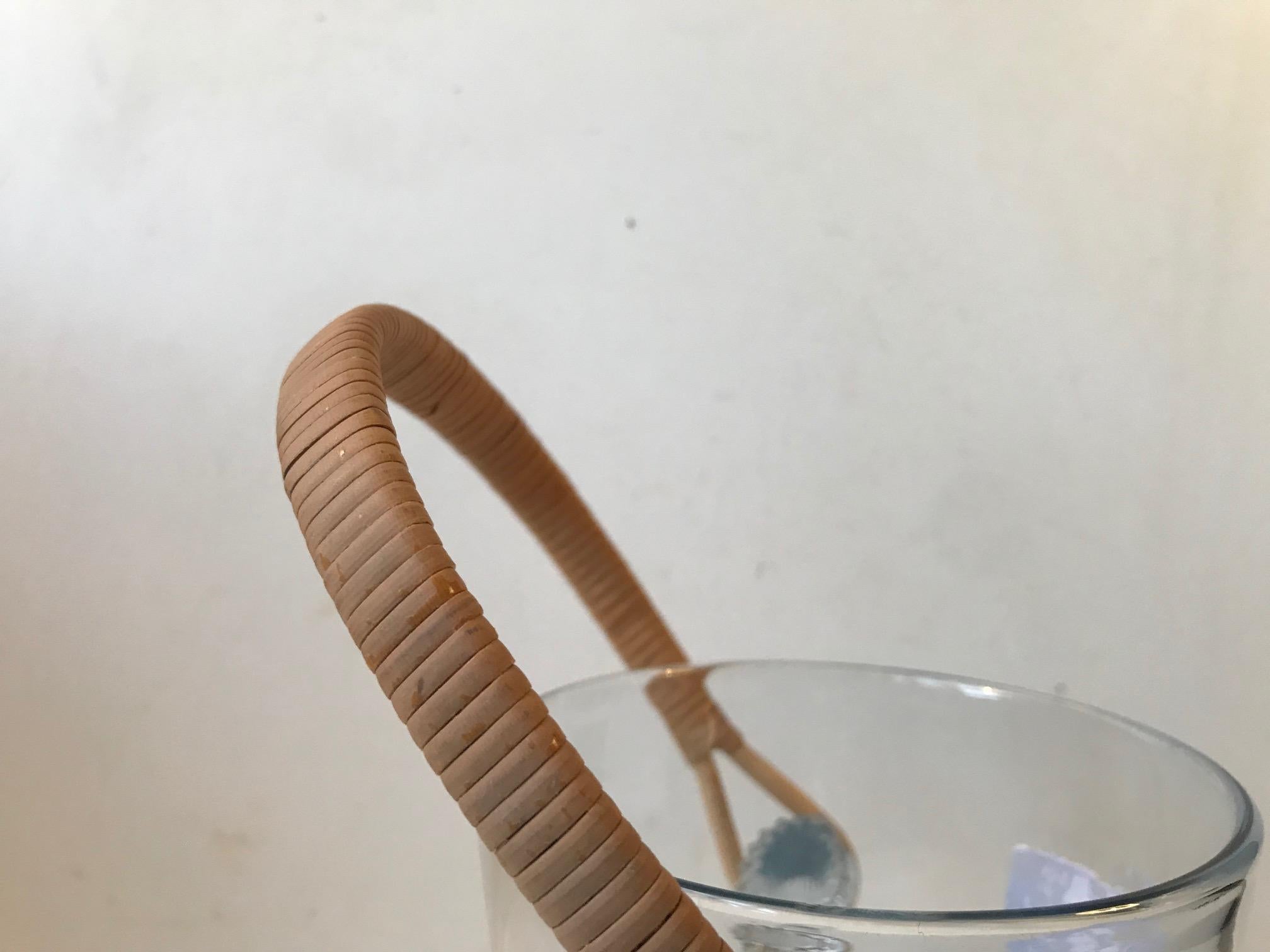 Ice bucket designed by Jacob E. Bang and manufactured by Holmegaard. Made from light blue toned handblown glass set with a rattan handle. A stainless steel ice tong from the period will accompany the ice bucket.