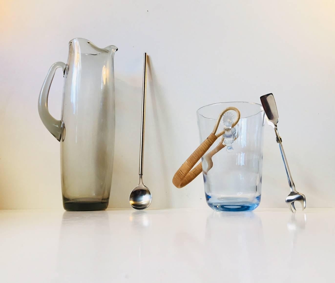 This set of four pieces consists of a large smoke glass pitcher designed by per Lütken, an ice bucket by Jacob E. Bang, both manufactured by Holmegaard and a stainless martini spoon and pitcher designed for and manufactured by Georg Jensen in