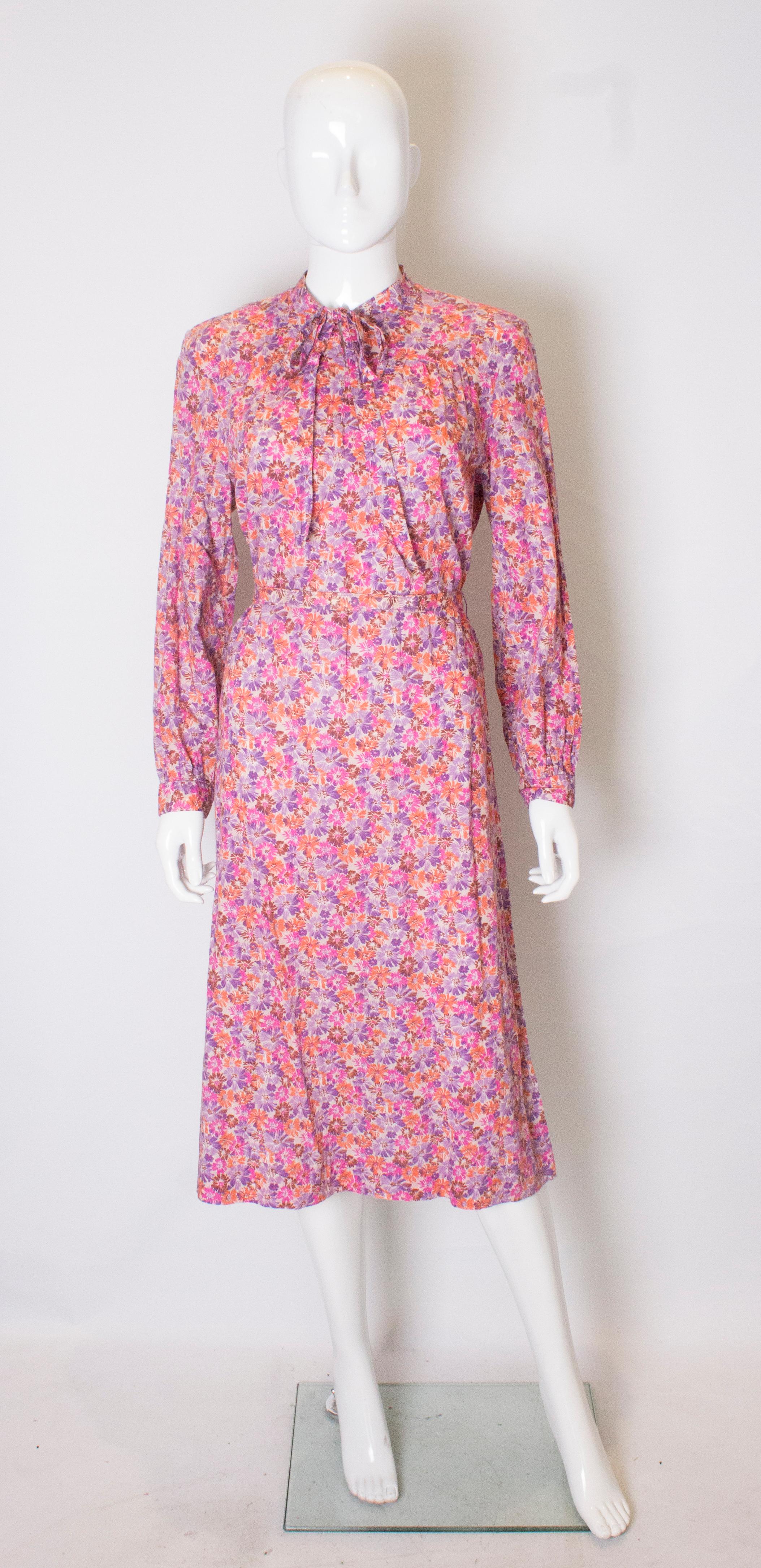 A pretty cotton print dress by Horrocks ( by appointment to Queen Elizabeth). The dress is in a pretty print of pink, purple, orang and brown. It has a central back zip, button cuffs and a self fabric belt.