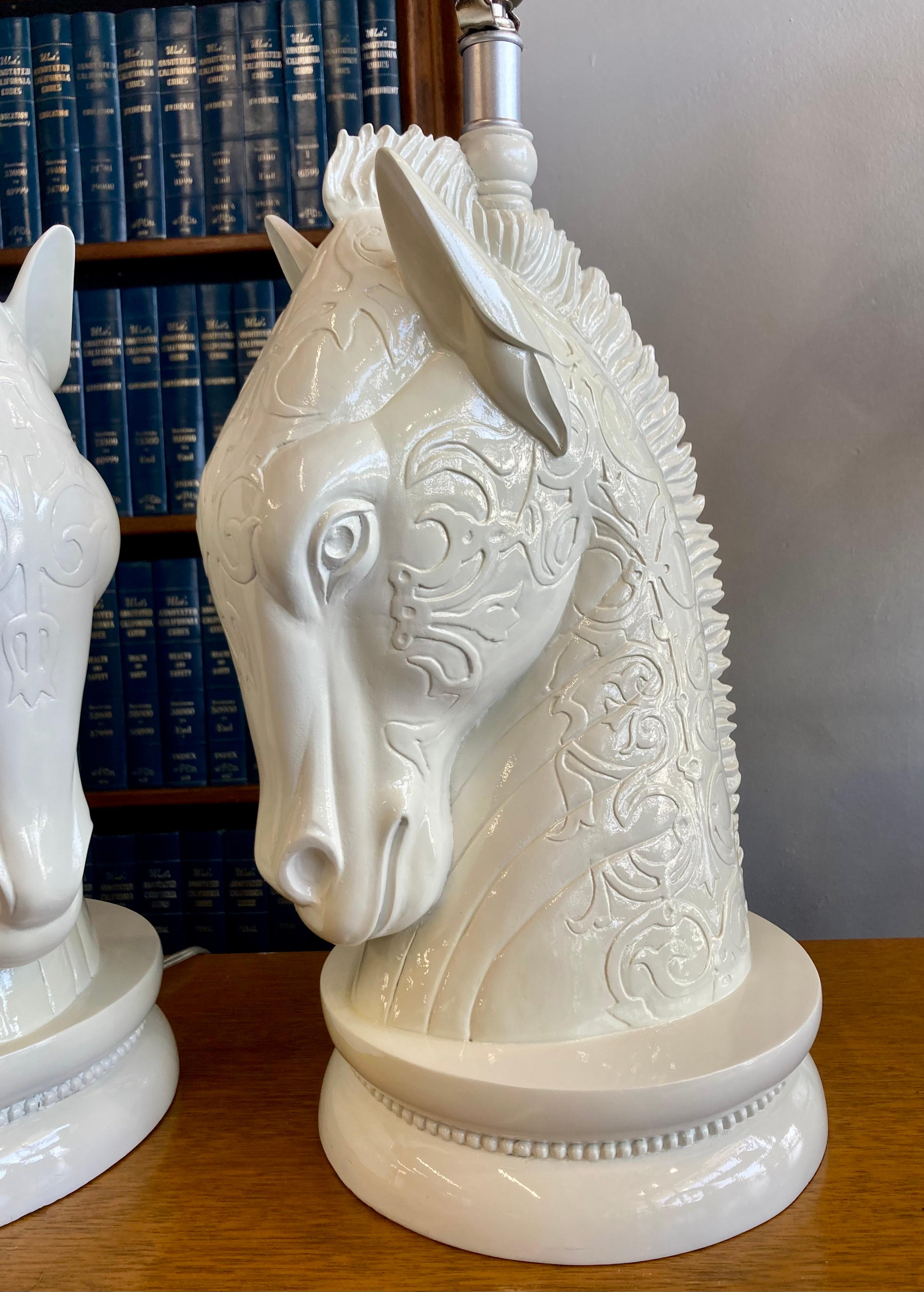 Vintage pair of decorative lamps in the shape of proud horses with a geometric relief pattern. An excellent piece of Mid-Century Modern/Hollywood regency interior style. Each lamp is topped in a two-headed horse finial. Sculpted horses are in
