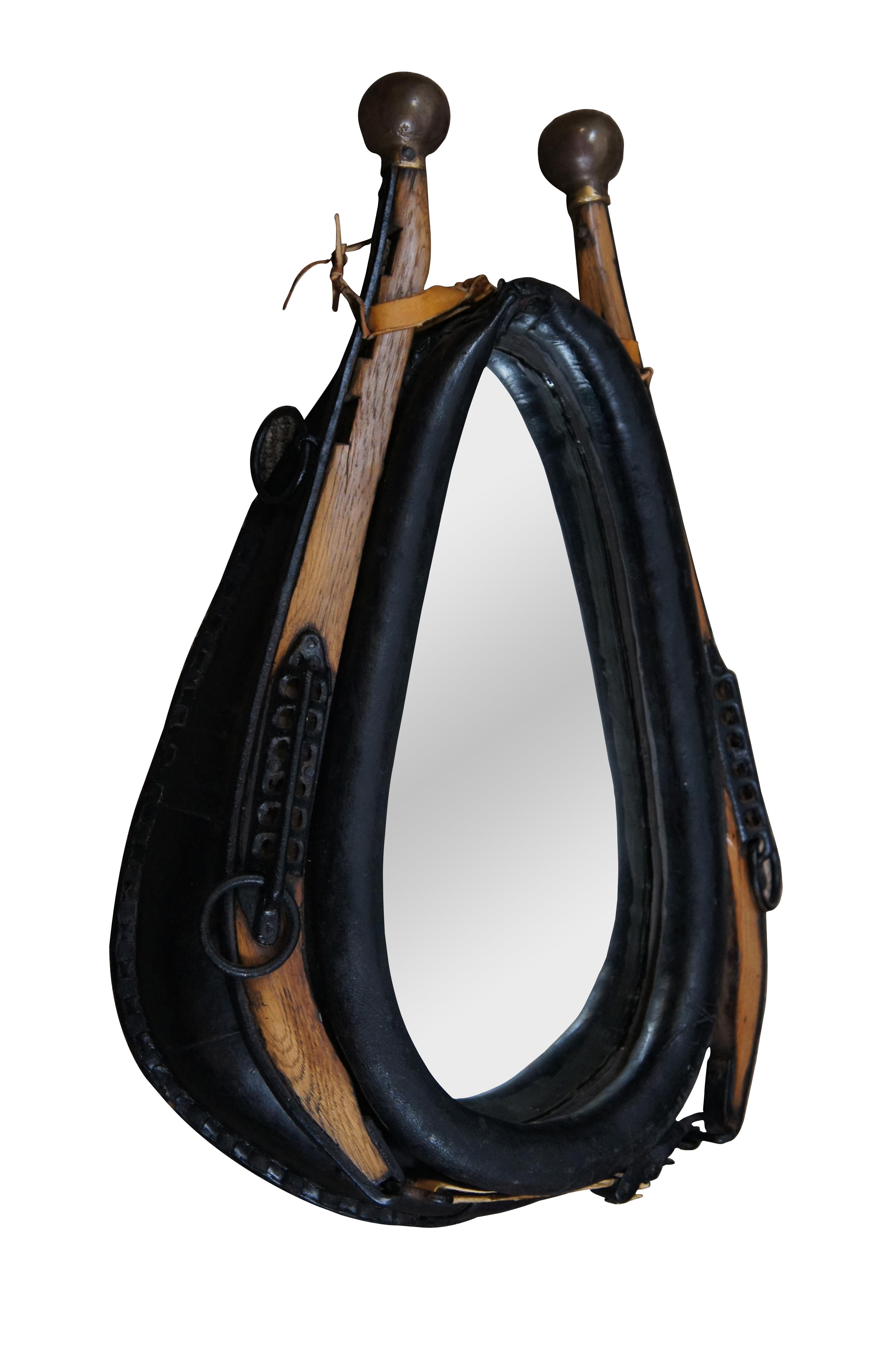Vintage rustic equestrian egg shaped wall mirror by the Carolina Mirror Corporation, framed in a wood and black leather horse yoke / driving collar with iron hardware and brass ball tips.