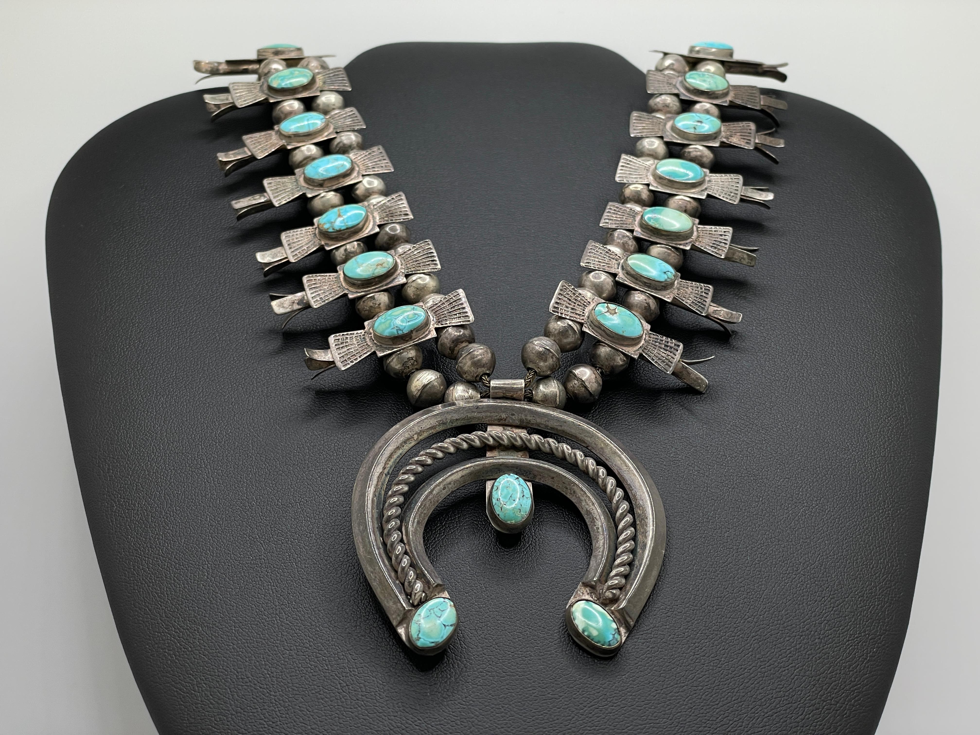 An authentic vintage Navajo Native American turquoise silver squash blossom necklace. This magnificent features a total of 23 natural blue turquoise cabochons, three of them set on the silver naja horseshoe pendant.

The necklace is has a double row