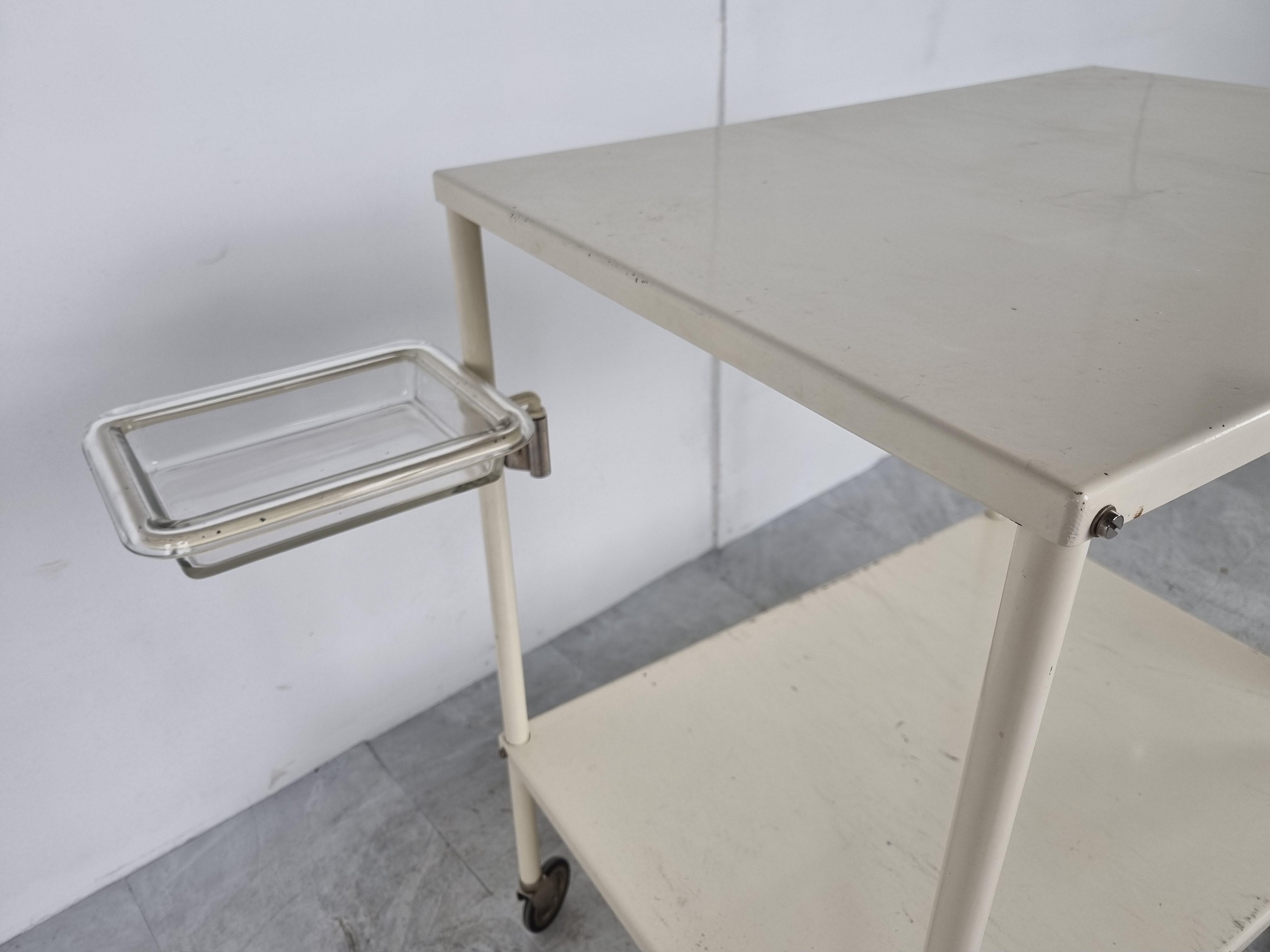 Vintage industrial hospital trolley or side table.

The trolley comes with the two original glass bowls.

This handy trolley was used by nurses to assist a patient during a hospital treatment or operation. It could carry instruments as well as