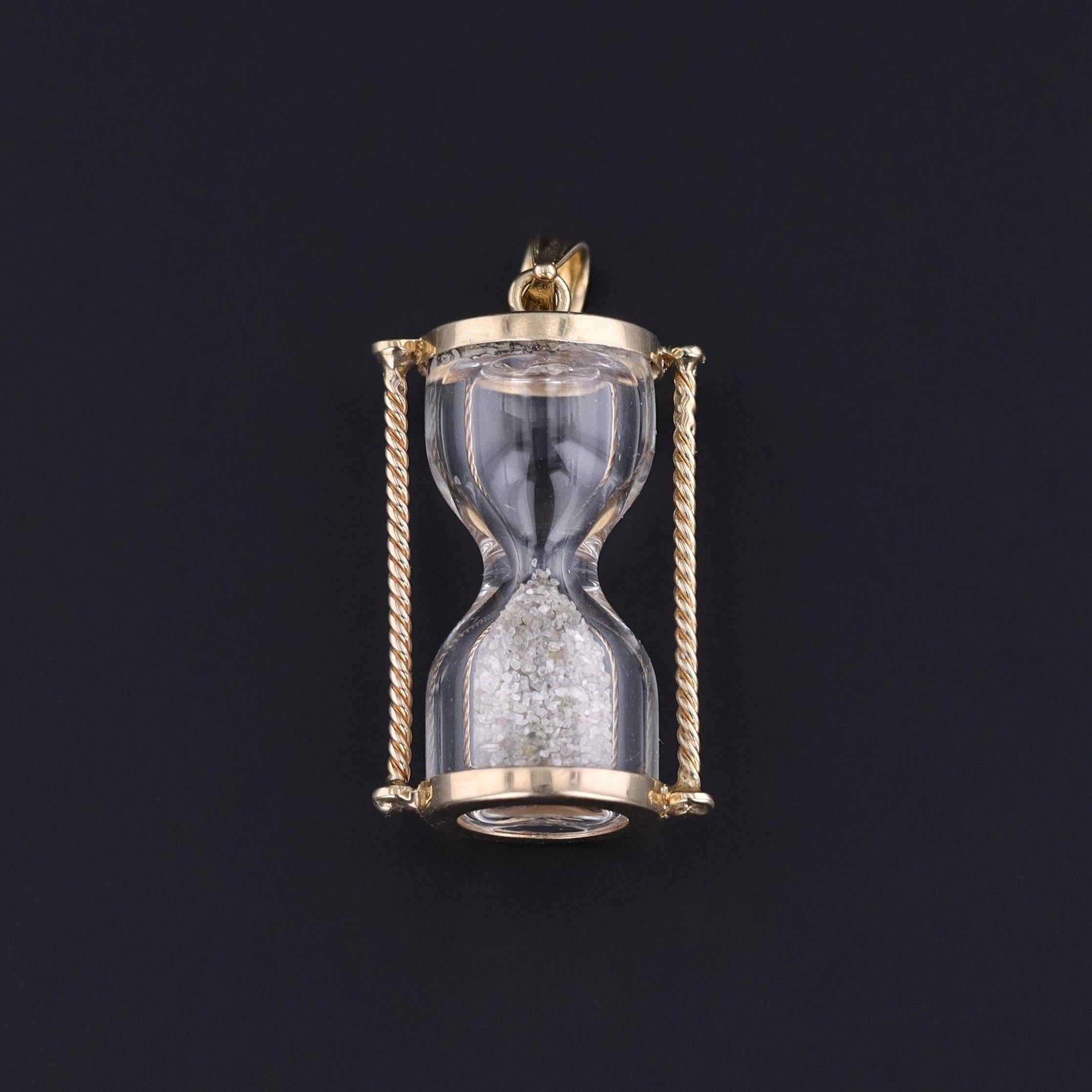 Questo charm vintage risale agli anni '60 e presenta una clessidra in oro 10k riempita di vetro o forse di piccoli frammenti di diamante.

Il pezzo misura 1,1 pollici dalla parte superiore della cauzione a quella inferiore per 0,55 pollici di