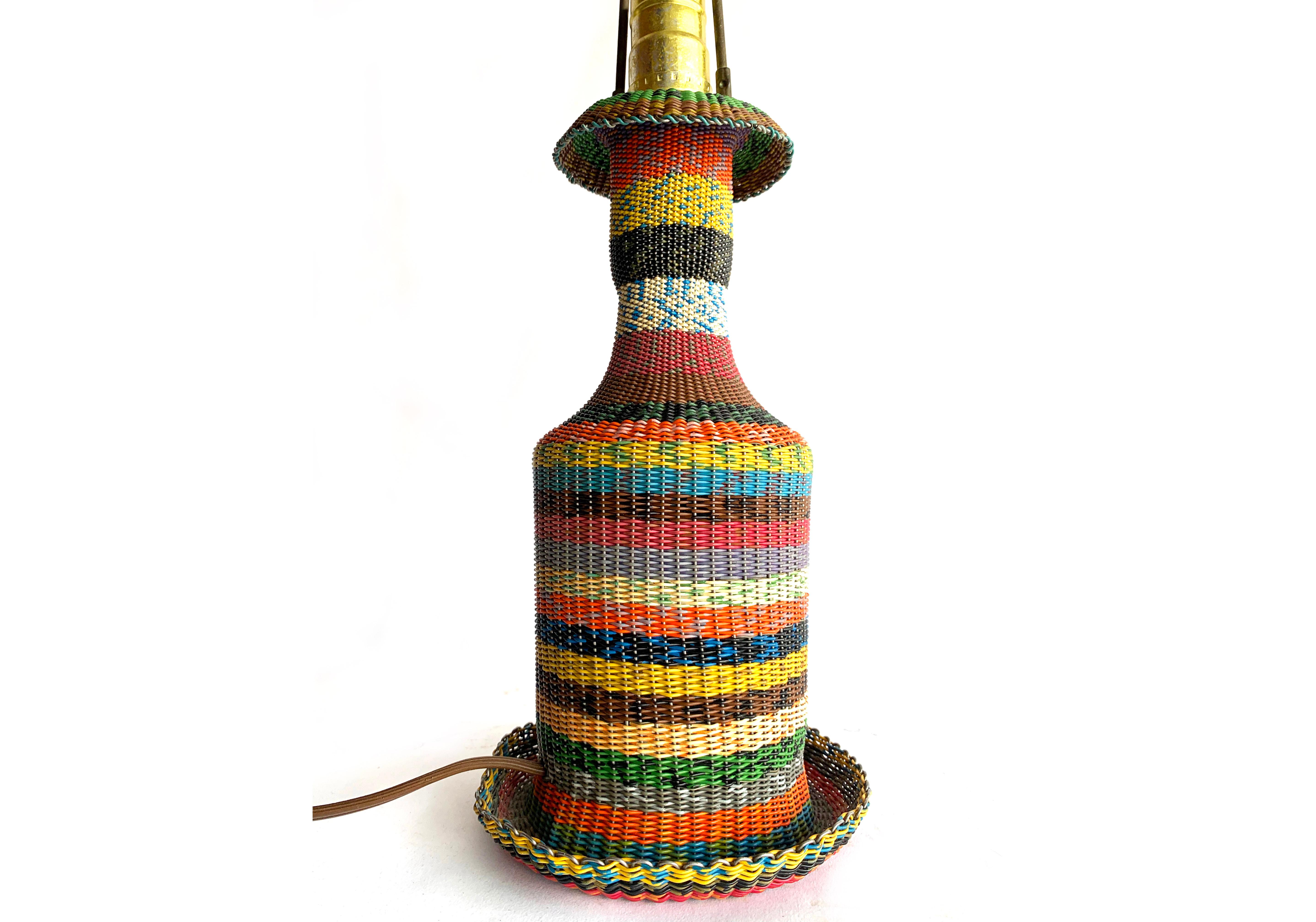Charming vintage woven-wire-covered glass bottle table lamp. The pattern and technique are based on traditional basket weaving and is considered a  unique piece of folk art. Vibrant color in the plastic 