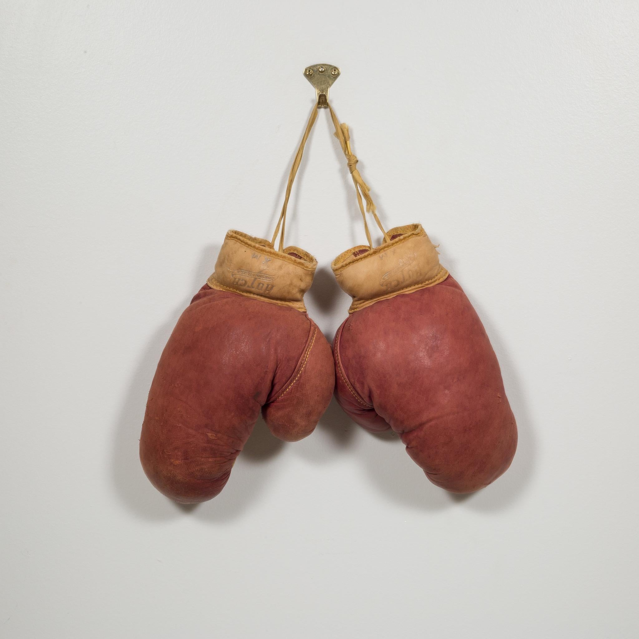 This is a original pair of vintage boxing gloves. The gloves are a maroon leather and light brown leather on the palm with light brown laces. The are both stamped 