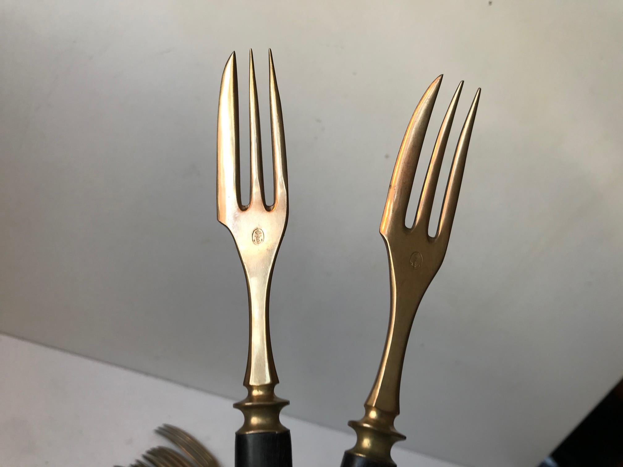 Rare complete set of so-called fork-knives in brass and black resin. The third spike of the fork doubles as a knife. The original intension was in regards to consuming cake and pastries in style. But they are also rather practical if you are