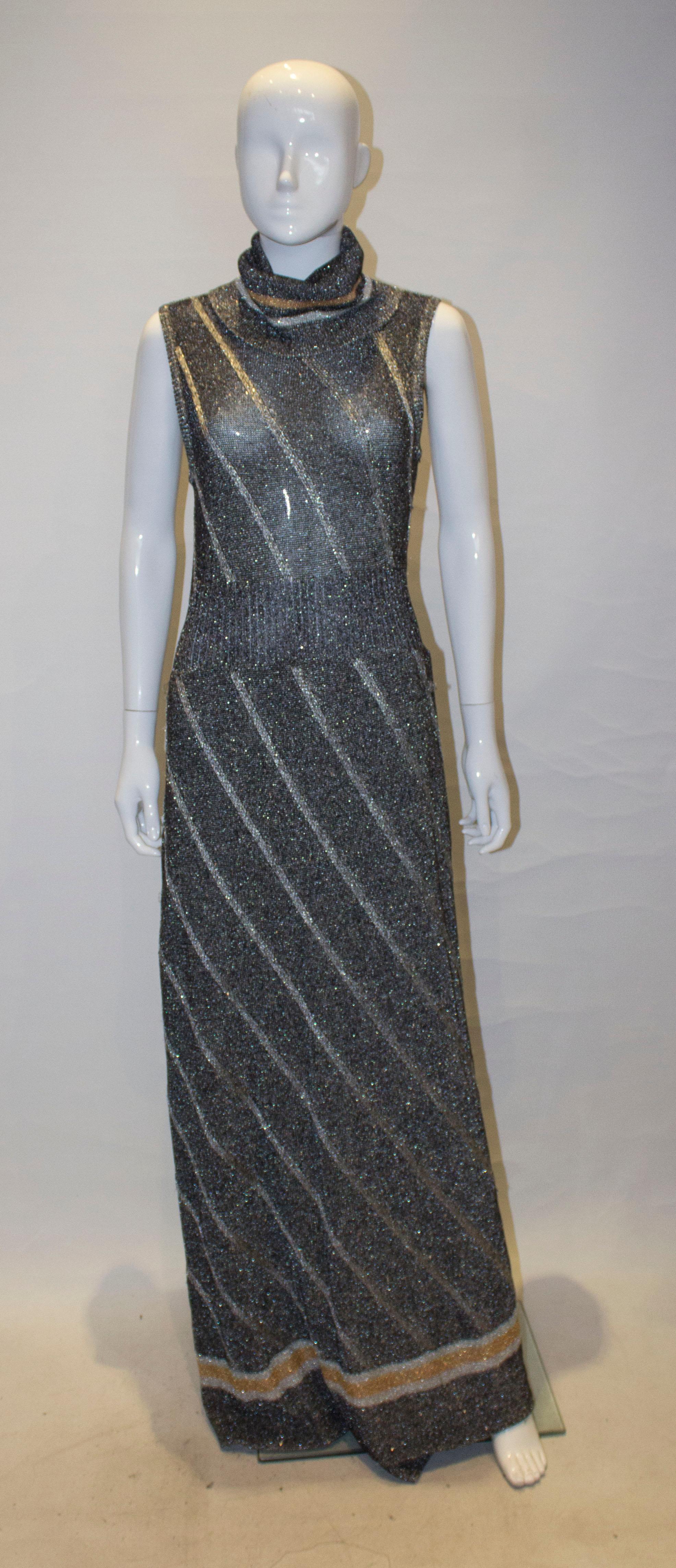 A chic knitted dress and jacket by Ian Peters. The dress is in a silver, gold and dark grey metallic mix , and has a roll neck and is lined from the waist down., and has a central zip fastening.  There is a matching cardigan /jacket with tie