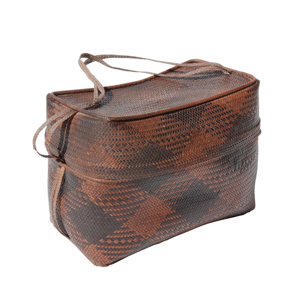 Scatola Iban con coperchio in rattan, Kalimantan occidentale, metà del XX secolo.
Una morbida scultura di pelle di rattan intrecciata e macchiata con un motivo a quadri marrone e nero disposto in diagonale. Una forma rettangolare con coperchio e un