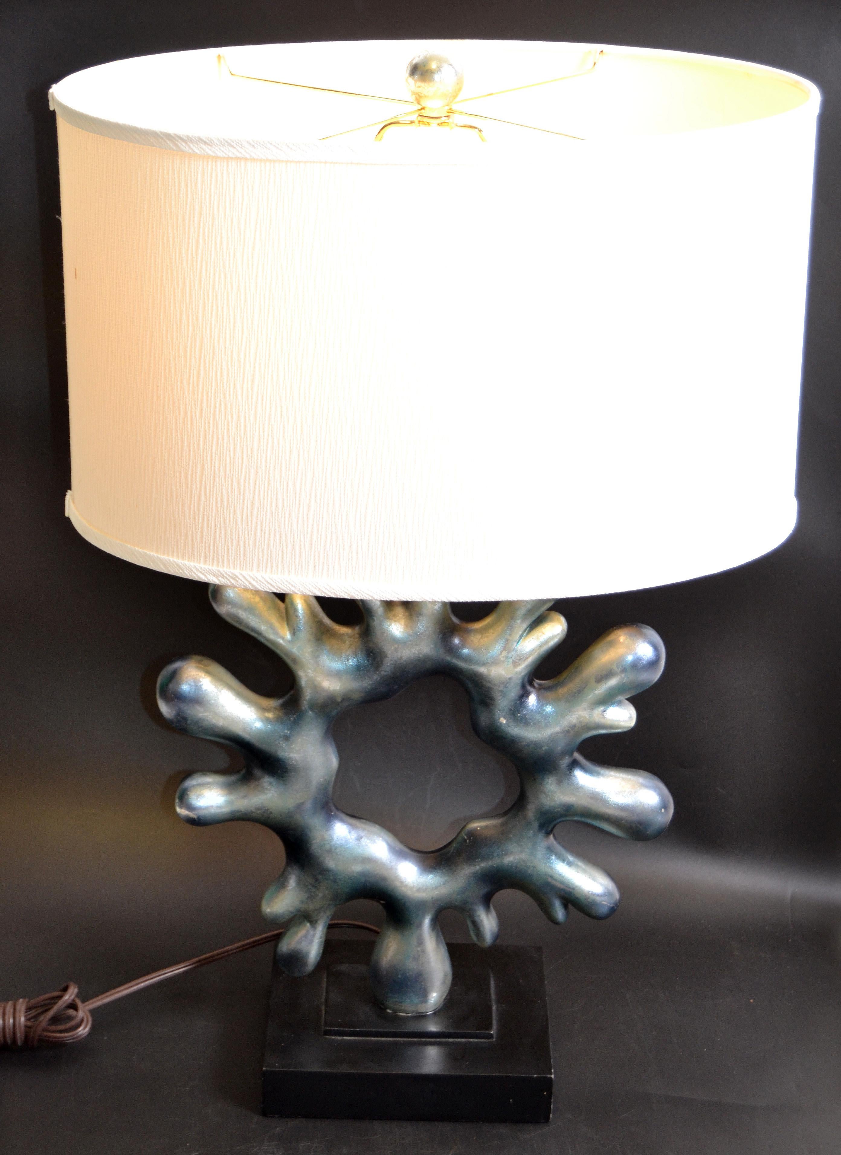 Mid-Century Modern biomorphic shape in abstract art metallic blue resin and wood table lamp with beige oval shade.
UL Listed in perfect working condition, wired for the US and takes a regular or LED bulb.
The biomorphic shape that seems to move as