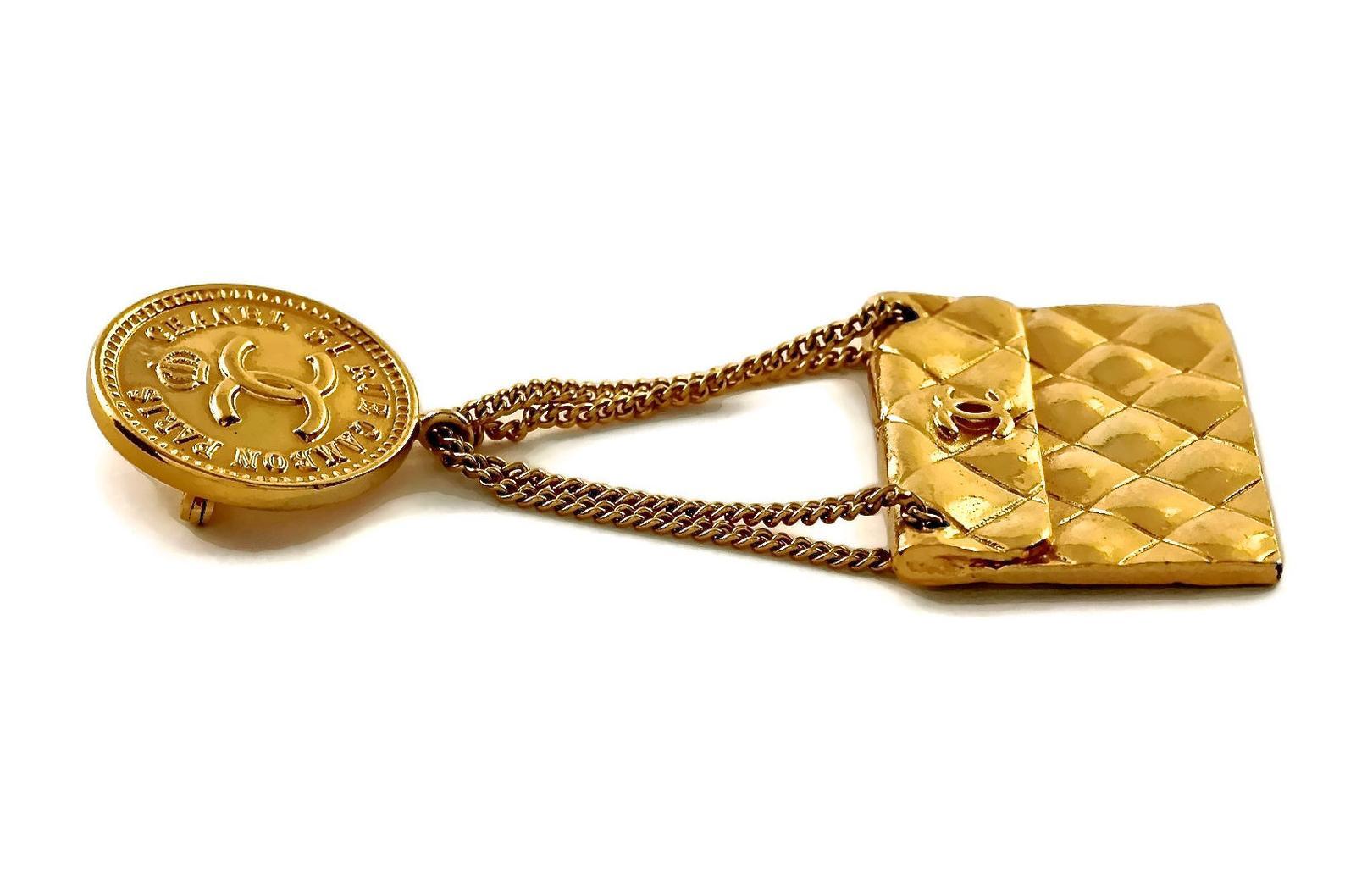 Vintage Iconic CHANEL Logo Coin Quilted Flap Purse Brooch

Measurements:
Height: 2.95 inches (7.5 cm)
Width: 1.33 inches (3.4 cm)

Features:
- 100% Authentic CHANEL.
- Coin with Chanel logo and address (top part).
- Dangling iconic Chanel 2.55