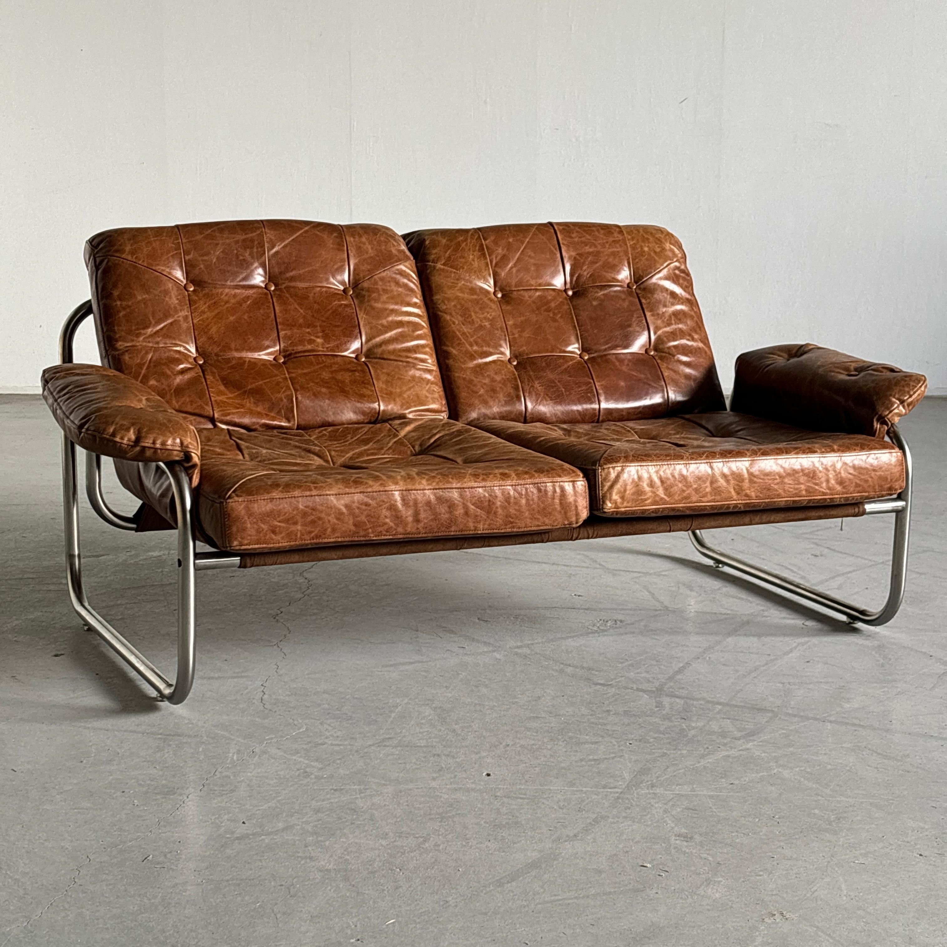 Sofá moderno sueco de dos plazas, de acero tubular cromado y tapicería de cuero marrón, de Johann Bertil Häggström para Ikea, años 70.

Esta pieza es uno de los productos IKEA de más éxito de los años 70, y un hallazgo muy raro.

Muy buen estado