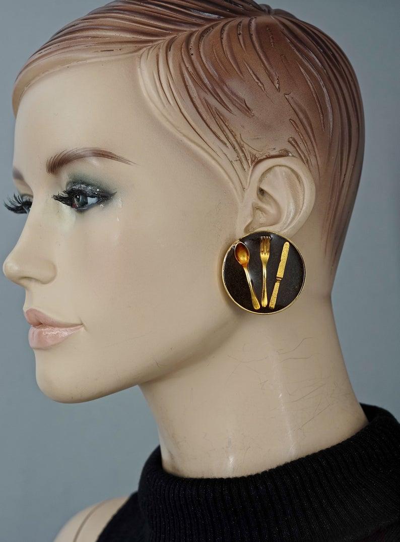 Vintage Iconic MOSCHINO Cutlery Earrings

Measurements:
Height: 1.57 inches (4 cm)
Width: 1.57 inches (4 cm)
Weight per Earring: 23 grams

Features:
- 100% Authentic MOSCHINO.
- Massive black resin disc earrings with embedded cutleries.
- Gold tone