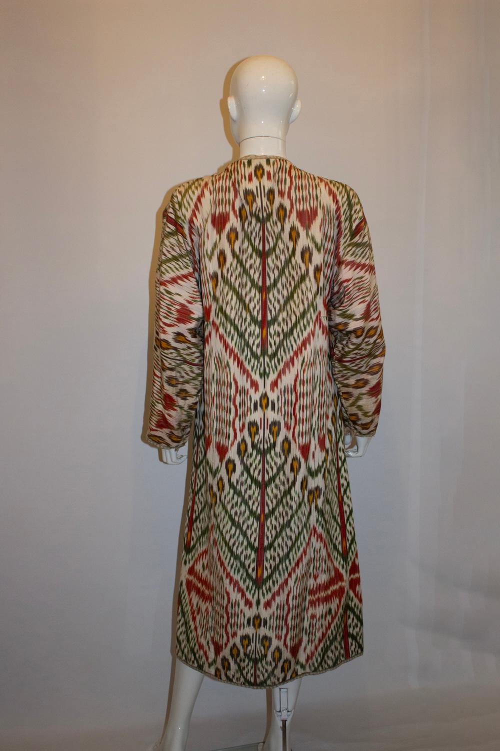 Un magnifique et saisissant manteau Ikat vintage. Le manteau a un fond ivoire avec un motif marron, jaune et vert. L'intérieur est doublé d'un coton imprimé rose et le manteau peut être porté à l'envers si vous le souhaitez. Il est ample, un peu