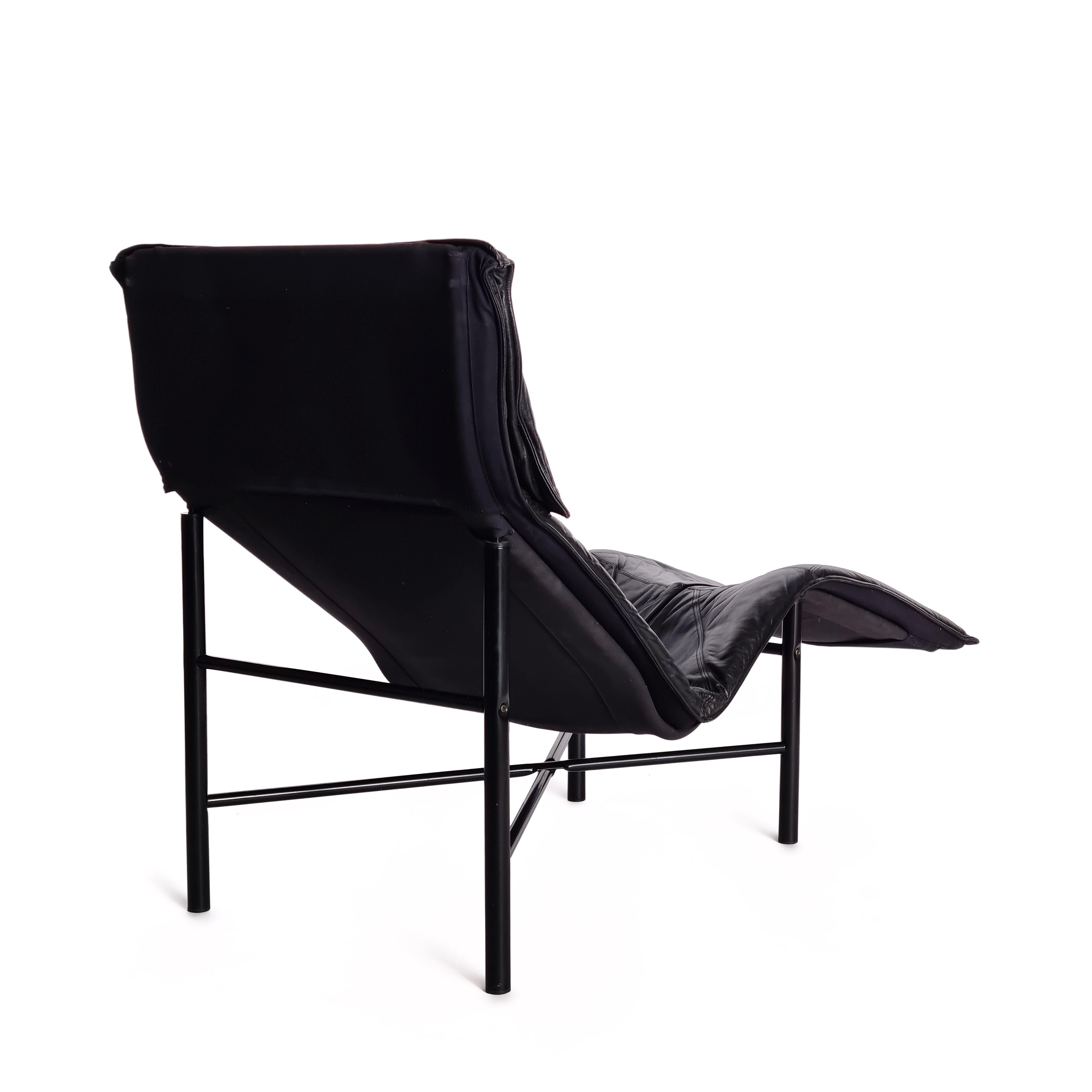 The stylish lounge chair features a sleek black steel frame paired with a black leather seat, offering both elegance and comfort. The chair remains in good and original condition, preserving its vintage appeal.