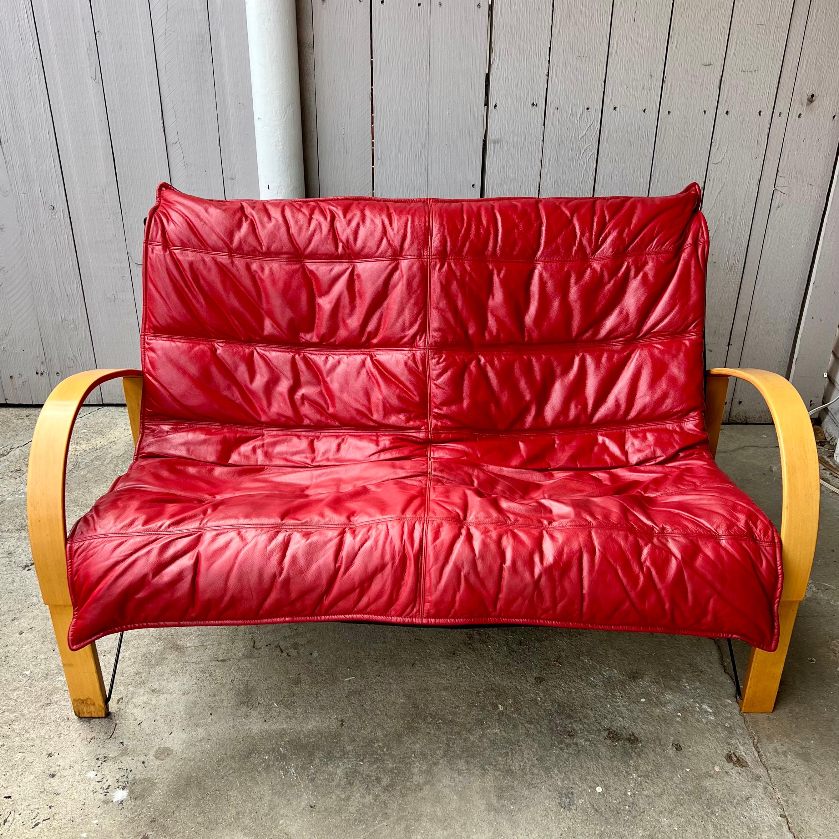 Designed by Tord Björklund in the 1980s for IKEA, this incredible, and durable loveseat boasts a bentwood birch frame with black metal accents and a supple removable red leather cover. Leather is in very good condition, very minimal marks and