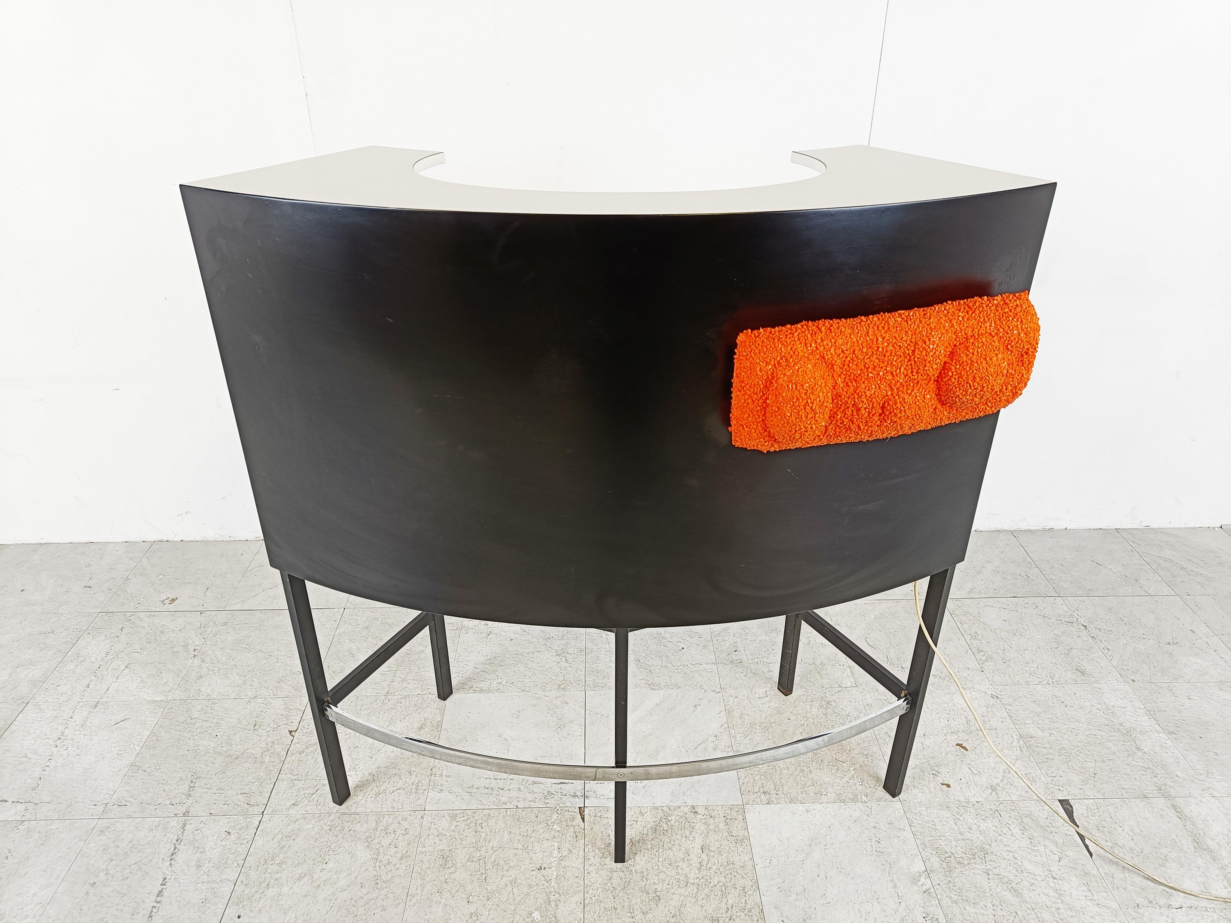 Striking seventies bar with a black lacquered wooden case, black metal and chrome base.

The inside of the bar provides plenty of storage space.

The bar also features a nice orange resin lamp.

Once illuminated it emits a soft welcoming