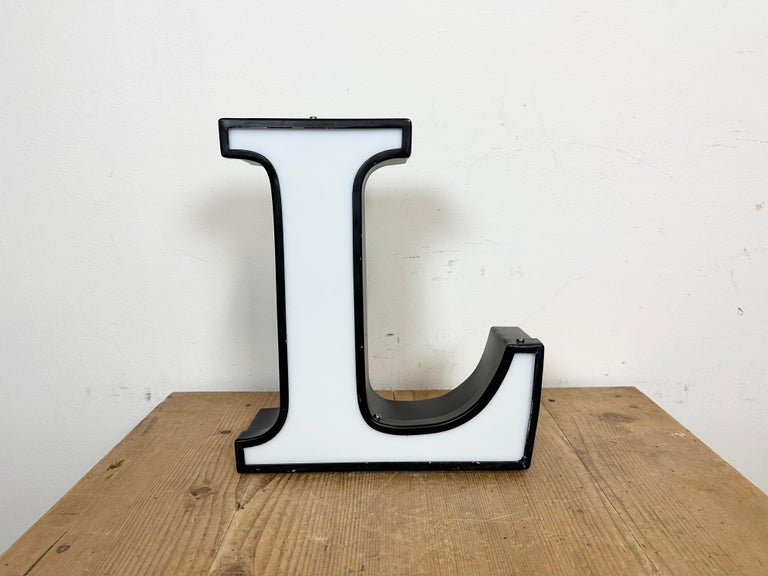 This vintage industrial illuminated letter L was made in Italy during the 1970s and comes from an old advertising banner. It features a black metal body and a white plexiglass cover. It is equipped with a LED strip. The letter can be used as a table