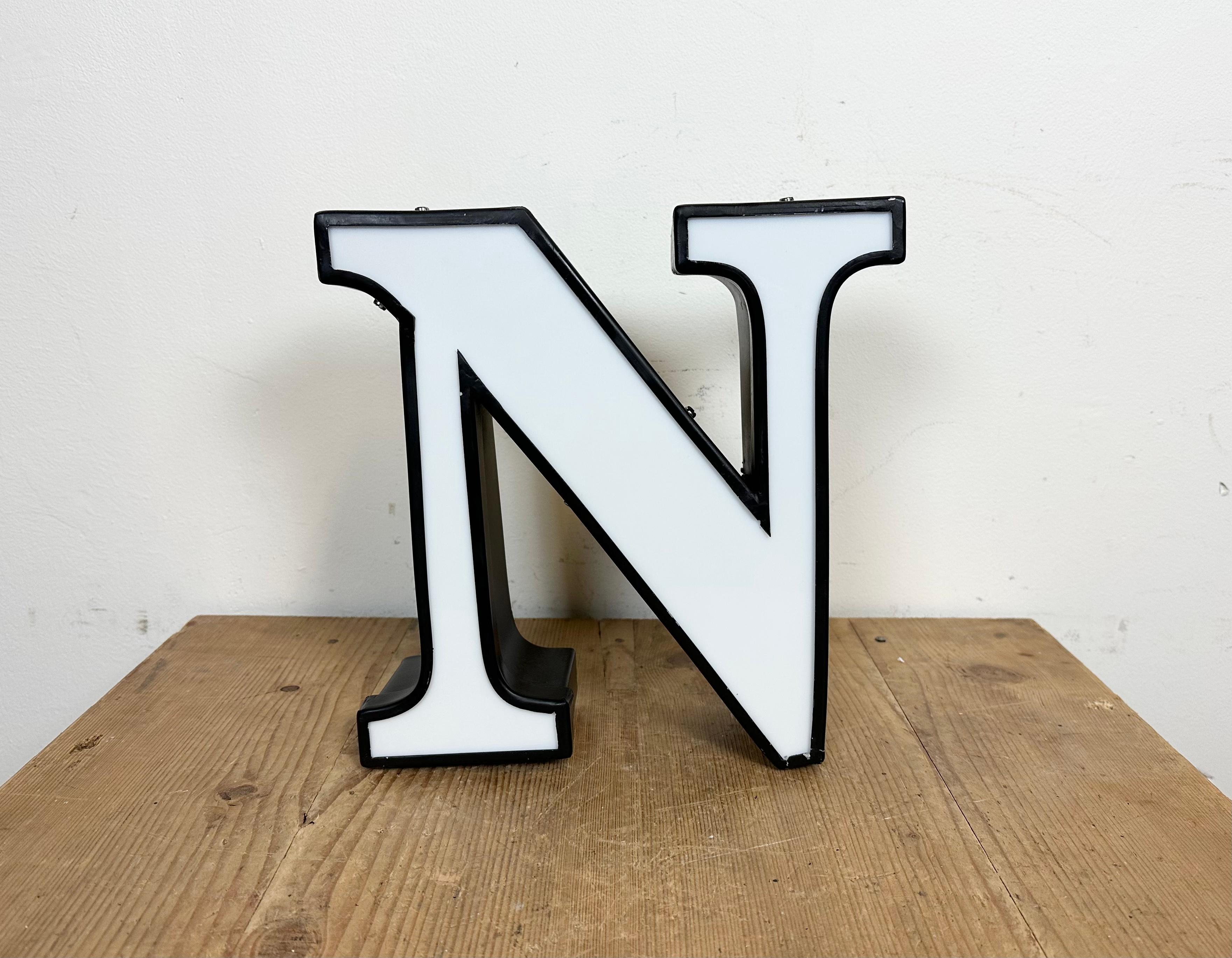 This vintage industrial illuminated letter N was made in Italy during the 1970s and comes from an old advertising banner. It features a black metal body and a white plexiglass cover. It is equipped with a LED strip. The letter can be used as a table