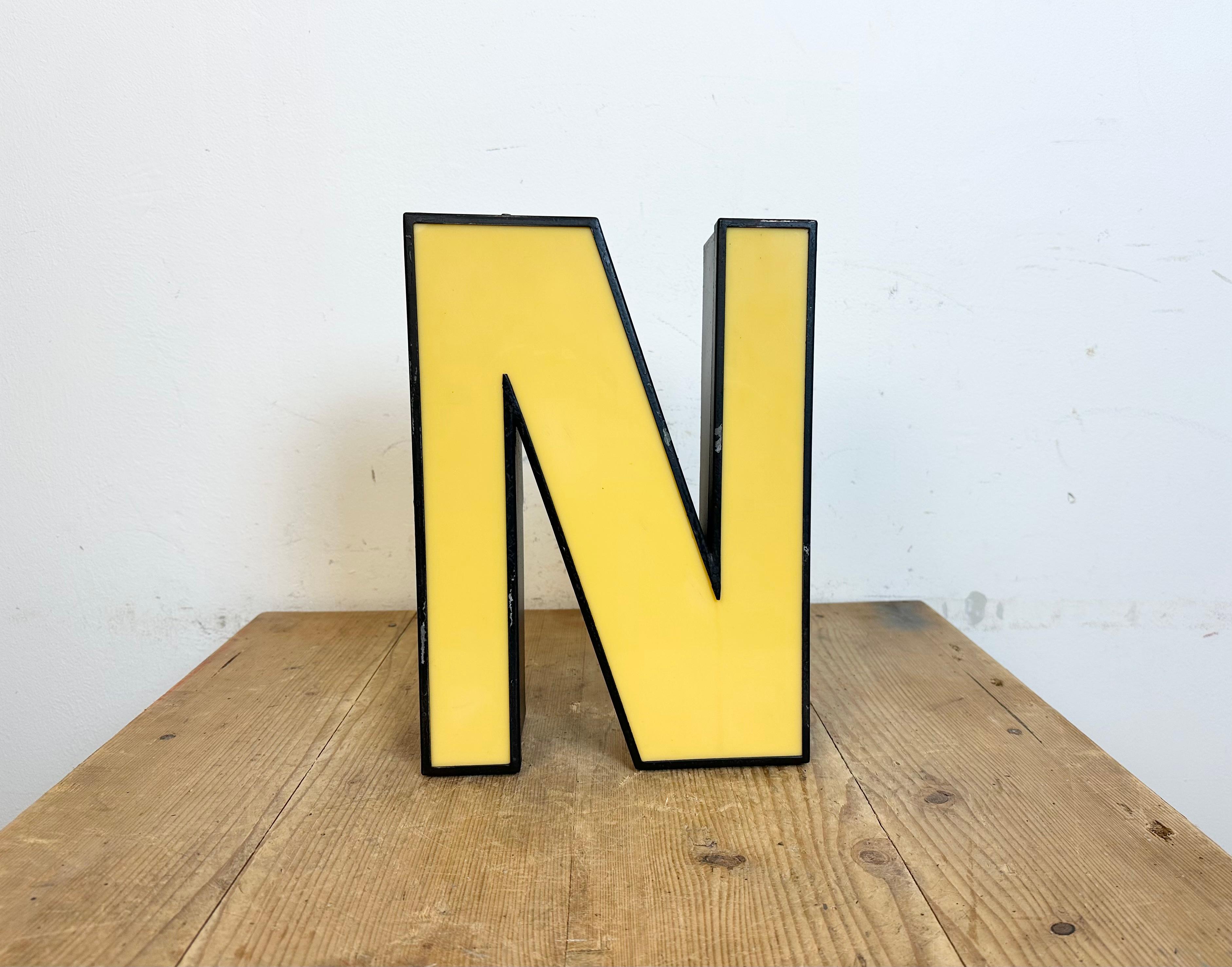 Esta letra L iluminada industrial vintage se fabricó en Italia en la década de 1970 y procede de un antiguo cartel publicitario. Presenta un cuerpo de metal negro y una cubierta de plexiglás amarillo. Está equipado con una tira de LED. La carta