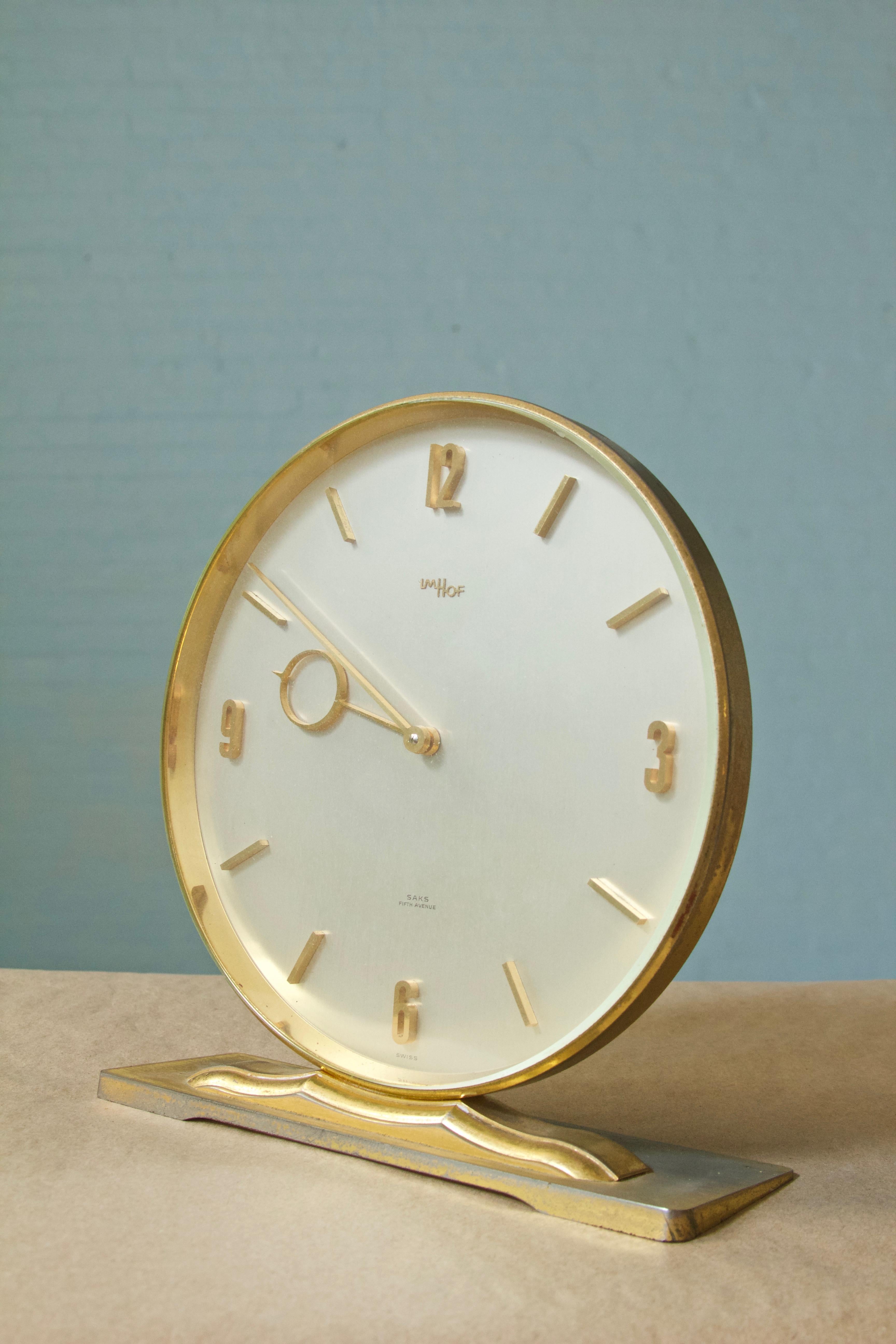 Stately, two-handed, Swiss 15 jewel, 8 day winding desk clock manufactured by Imhof for Saks Fifth Avenue- early 1960s.
Polished brass, splayed circular clock face, with applied solid brass time indicators. Imhof, a maker regarded as 