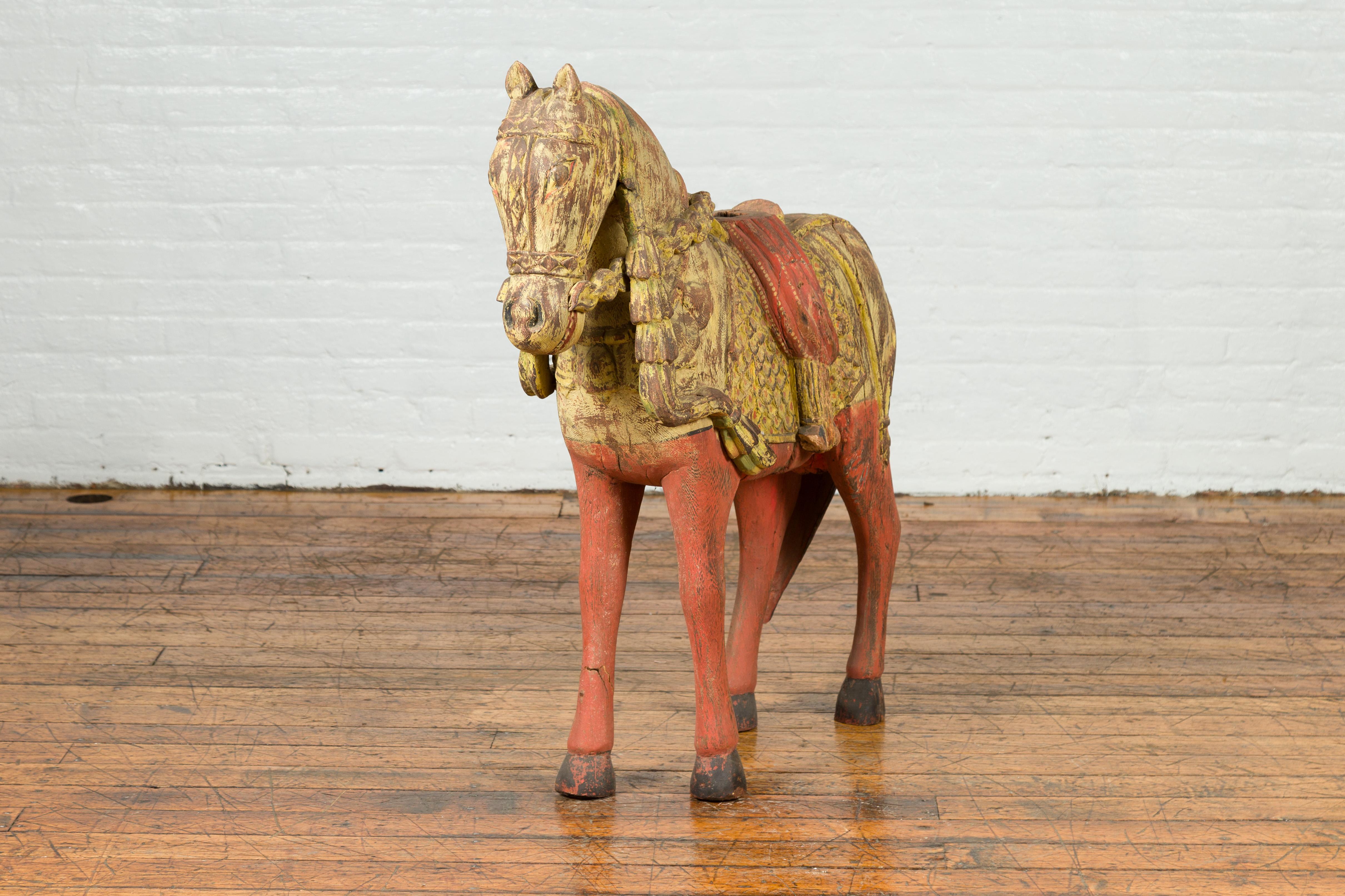 An Indian vintage carved and painted wooden horse sculpture from Madras with distressed patina. Born in the Indian state of Tamil Nadu during the midcentury period, this carved horse charms us with its yellow and red painted finish and distressed