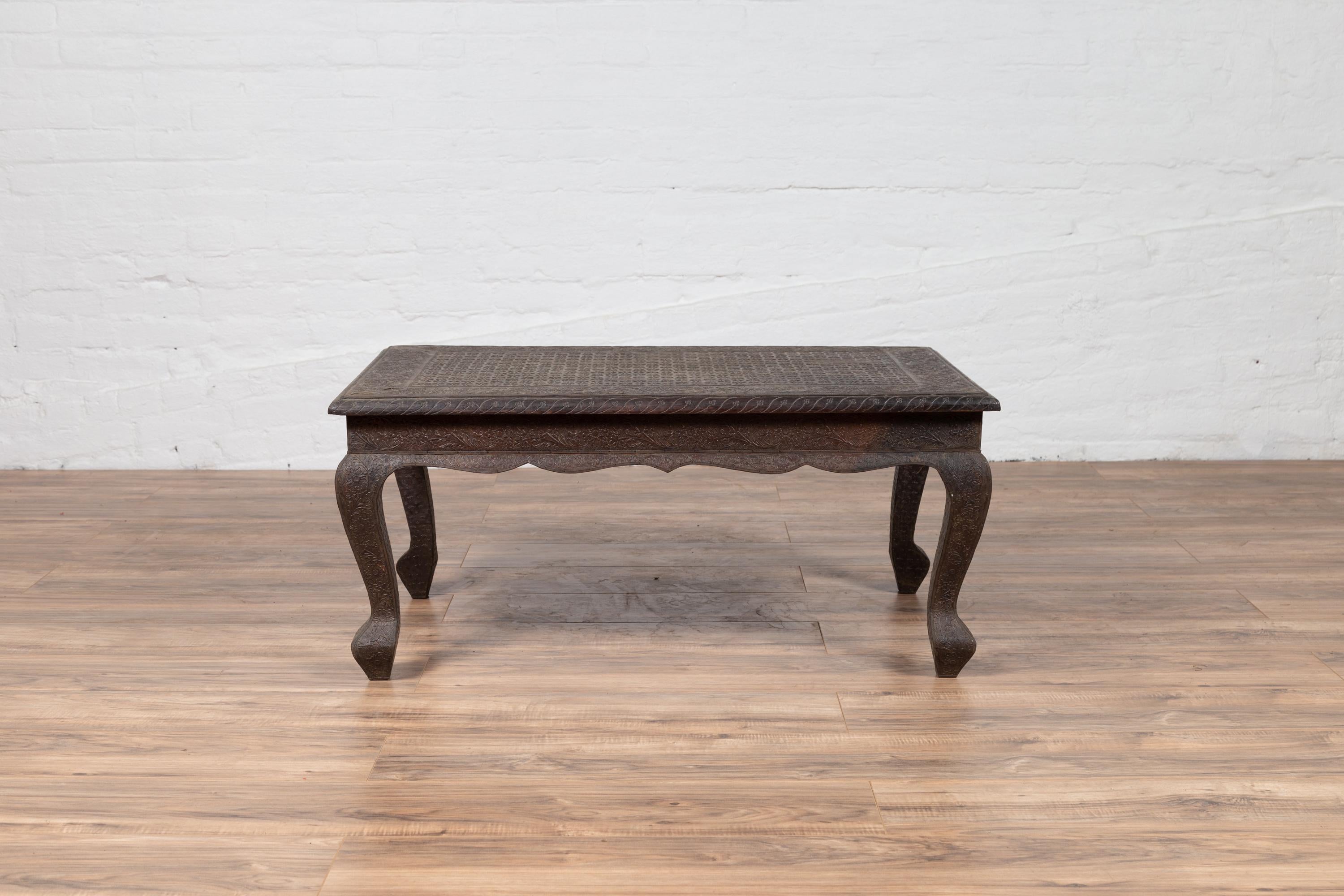 An Indian vintage coffee table from the mid-20th century, with handmade brushed metal patina over wood, hand-etched floral motifs and cabriole legs. This mid-20th-century Indian vintage coffee table is a striking example of craftsmanship and
