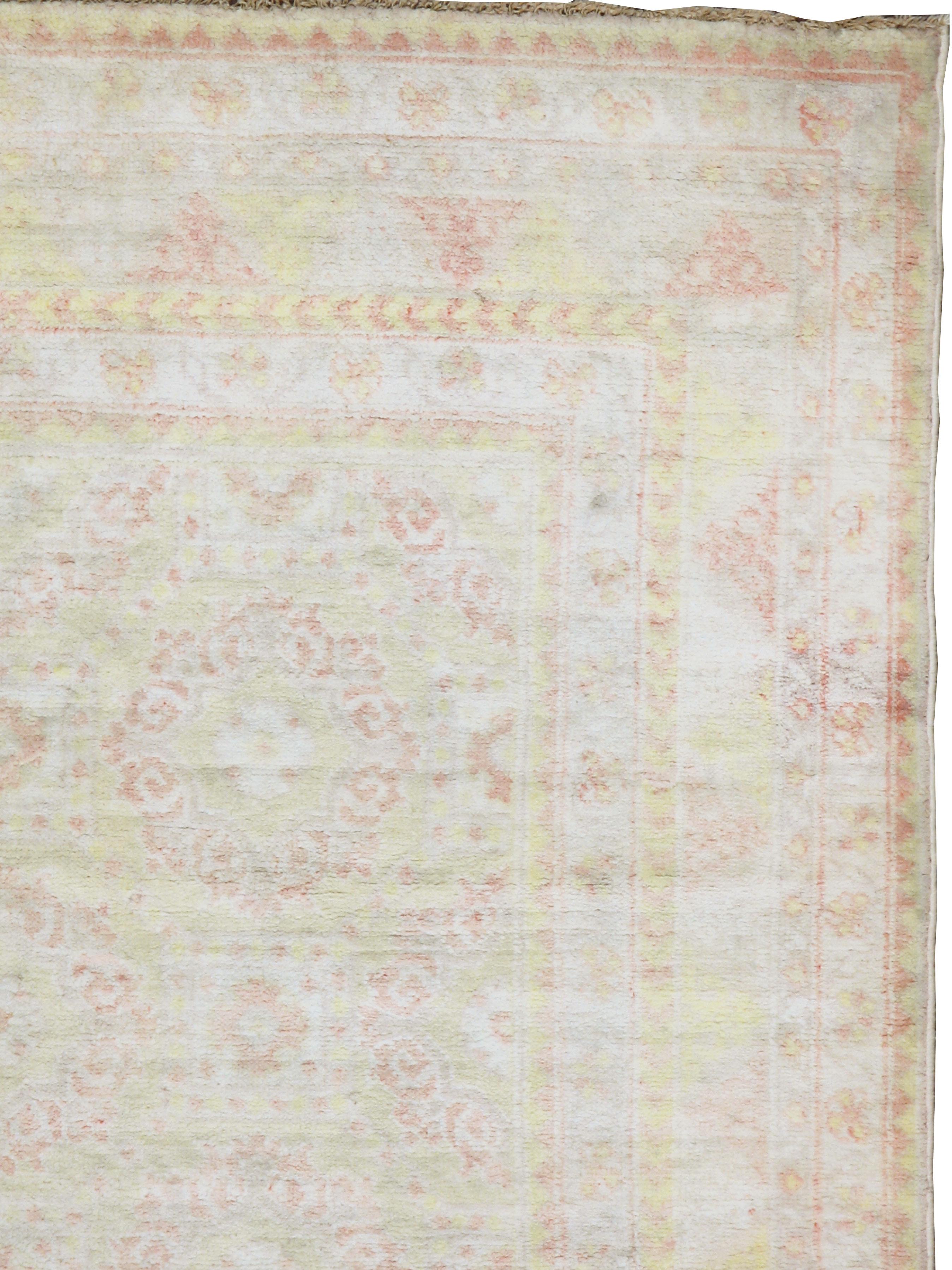 A vintage Indian cotton Agra rug from the mid-20th century. This northern Indian scatter employs a yellow, ivory, and green soft tonality to better display the round foliate wreath field pattern in soft pink. The yellow accents in the borders are a