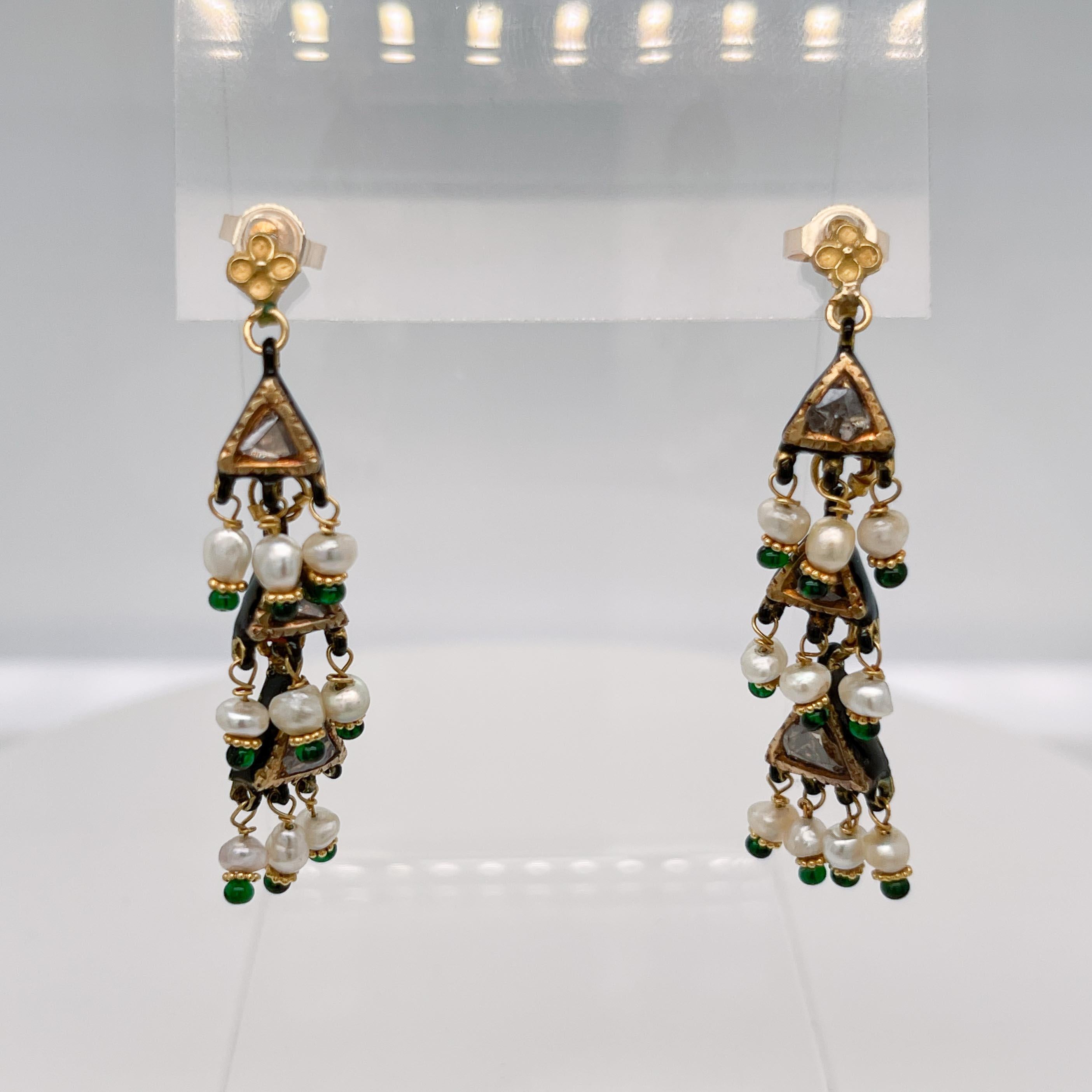 A fine pair of Indian gold and polki diamond dangle earrings.

With polki diamonds bezel-set in triangular 14k gold sections and tiny seed pearls and emerald beads on twisted gold wire.

Decorated with a black enamel pattern to the reverse of each