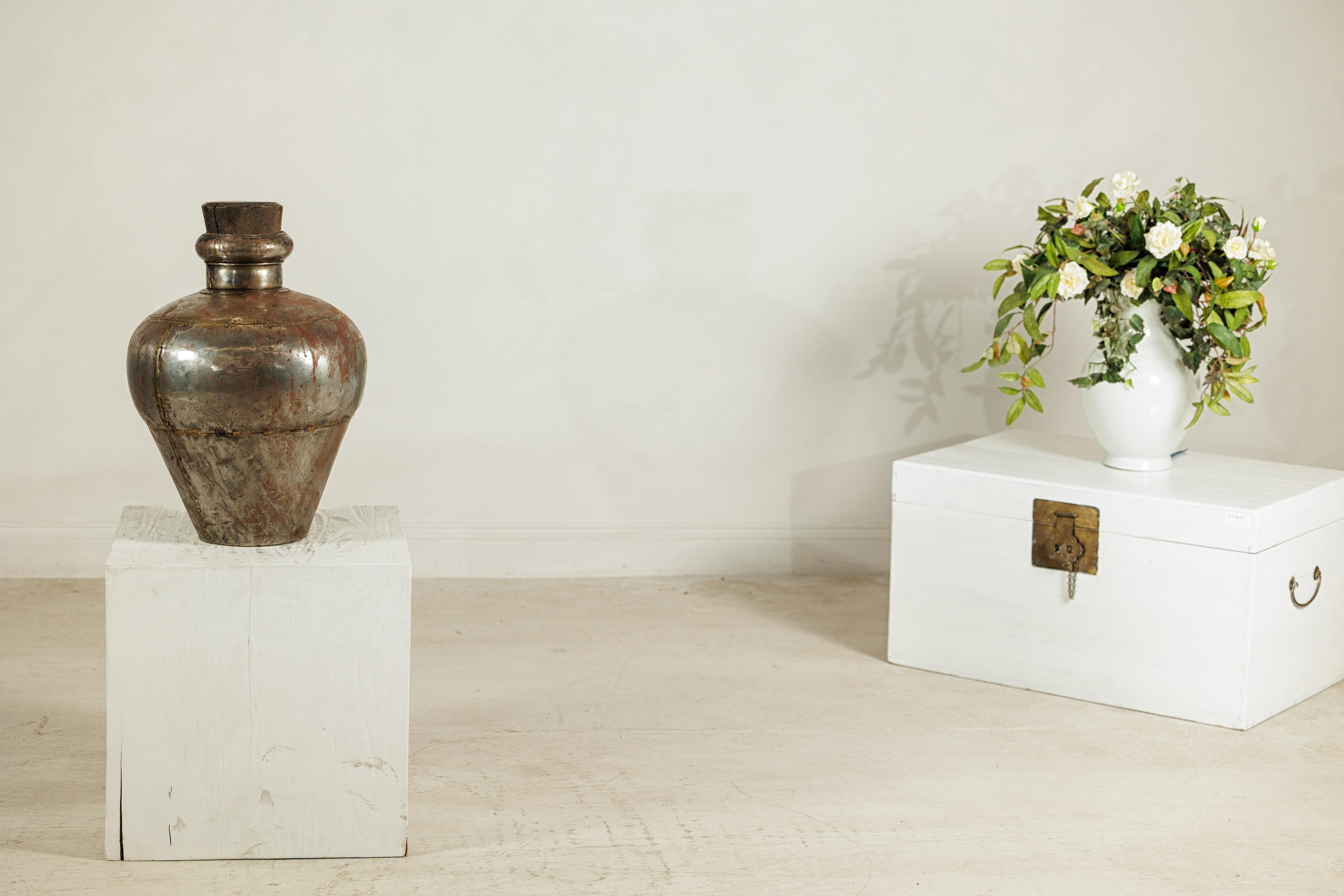 Esta vasija de agua de metal indio vintage es un sorprendente ejemplo de artesanía utilitaria elevada por el tiempo y la pátina. Totalmente hecha a mano, la pieza presenta un hombro redondeado que se estrecha hasta una base cónica, sus costuras