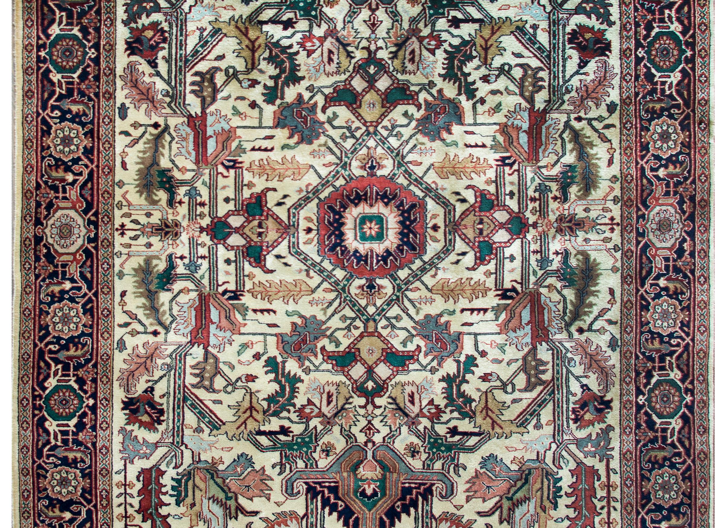 A beautiful vintage Indian Heriz-style rug with a large-scale all-over mirrored stylized floral and leaf pattern woven in pink, crimson, green, indigo, and gold, and set against a cream colored background.  The border is equally as stunning, with a