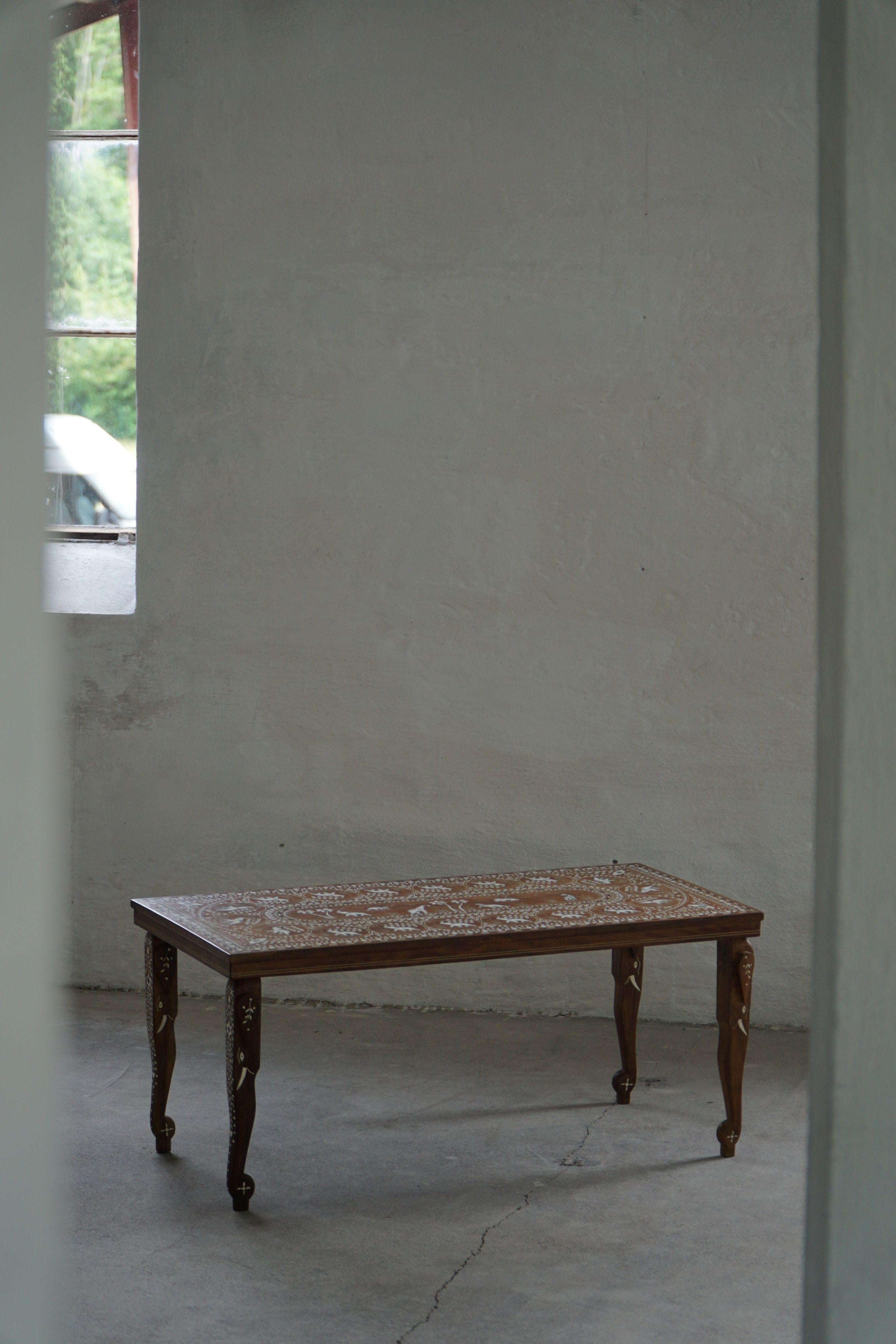 Ein bezaubernder anglo-indischer Couchtisch aus der Mitte des 20. Jahrhunderts, reich verziert mit Elefantenmotiven, die sowohl in die Tischplatte eingelegt sind als auch an den Beinen dezent wiederkehren. Die Kunstfertigkeit spiegelt das Erbe der