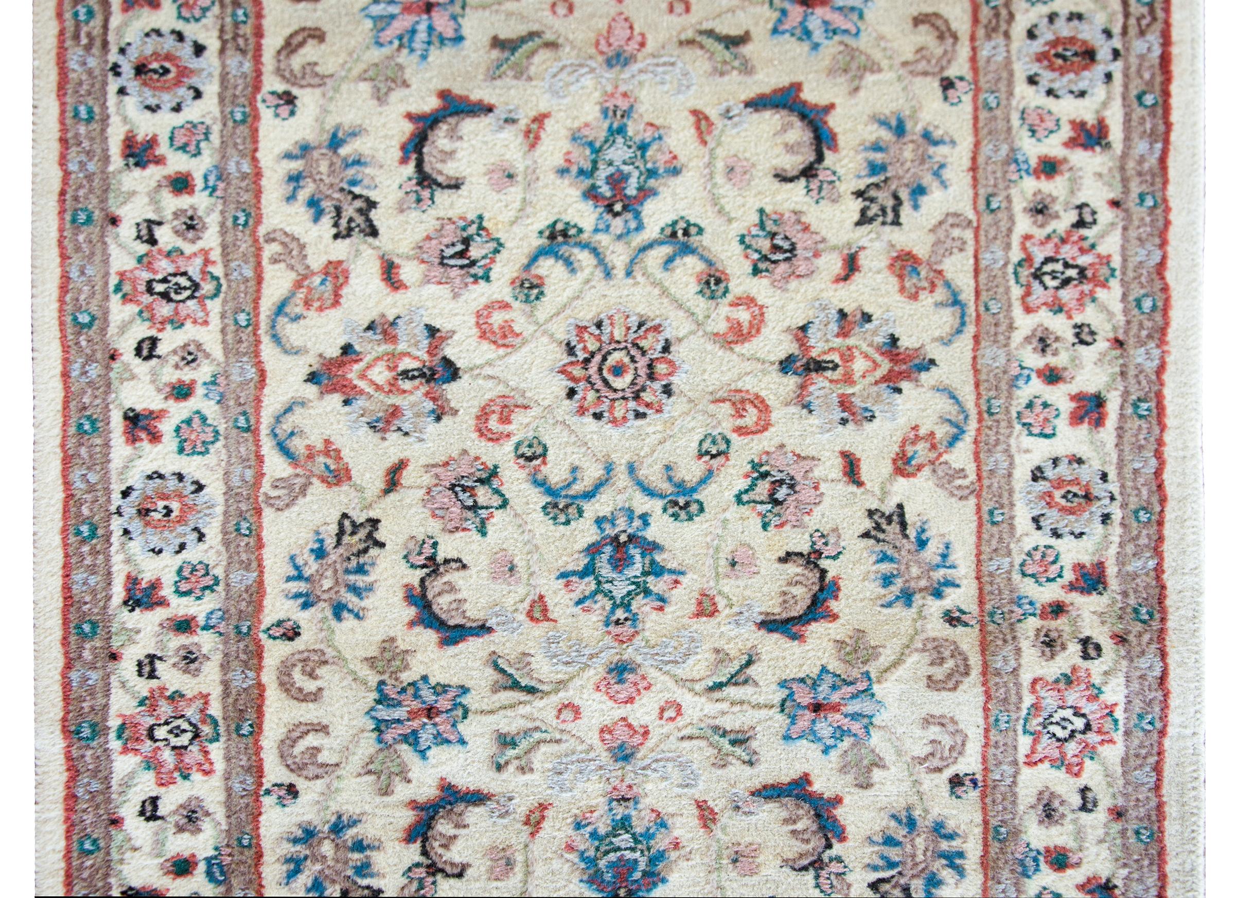 A wonderful late 20th century Indian rug with a beautiful hand-woven floral and scrolling vine pattern woven in crimson, pink, indigo, and gray against a cream colored background. The border is simple with a similar floral pattern as the field.