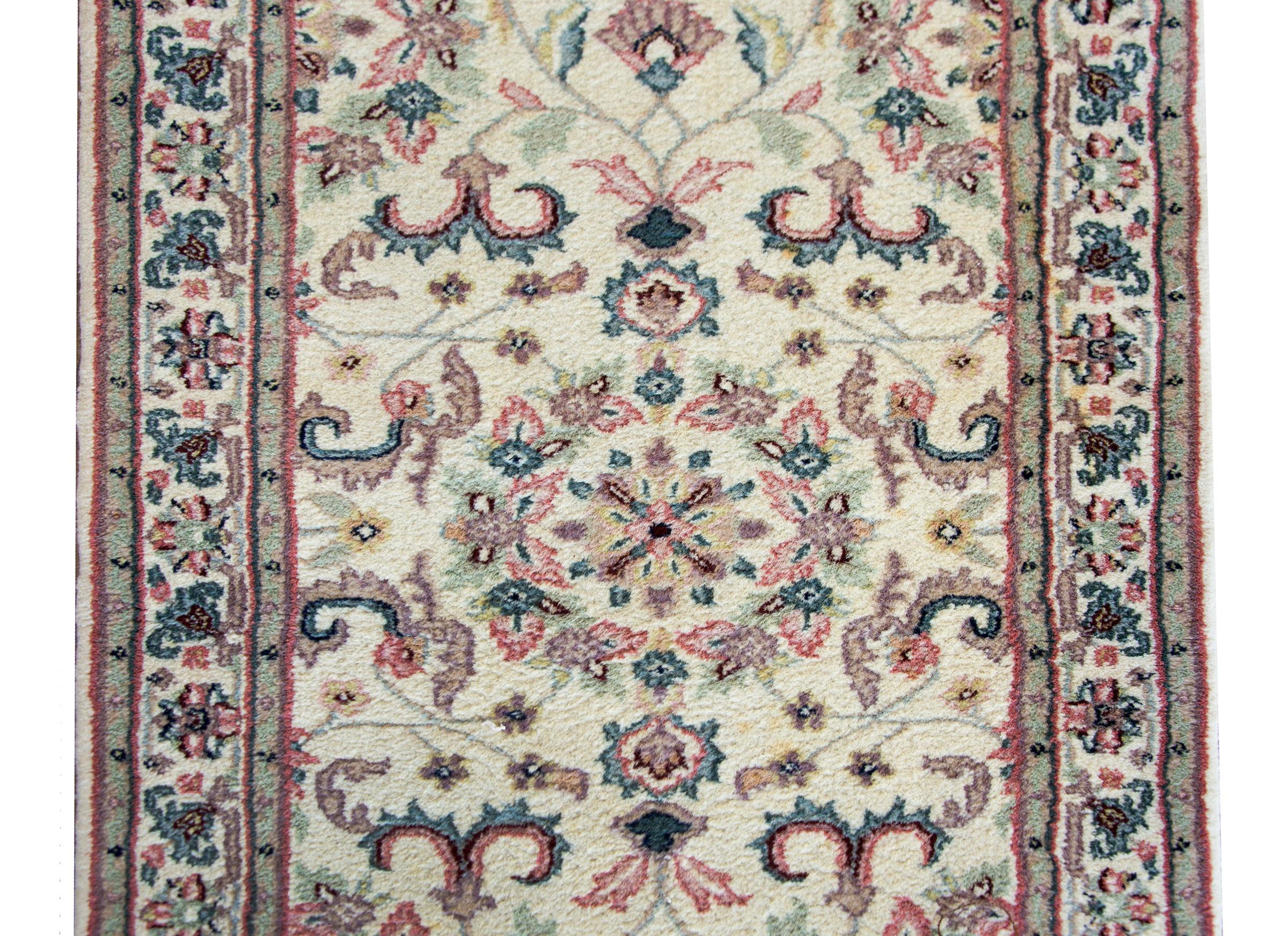 A late 20th century hand-knotted Indian runner with a Persian pattern containing several mirrored stylized floral and scrolling vine patterns surrounded by a simple border with more flowers and scrolling vines, and all woven in pinks, yellows,