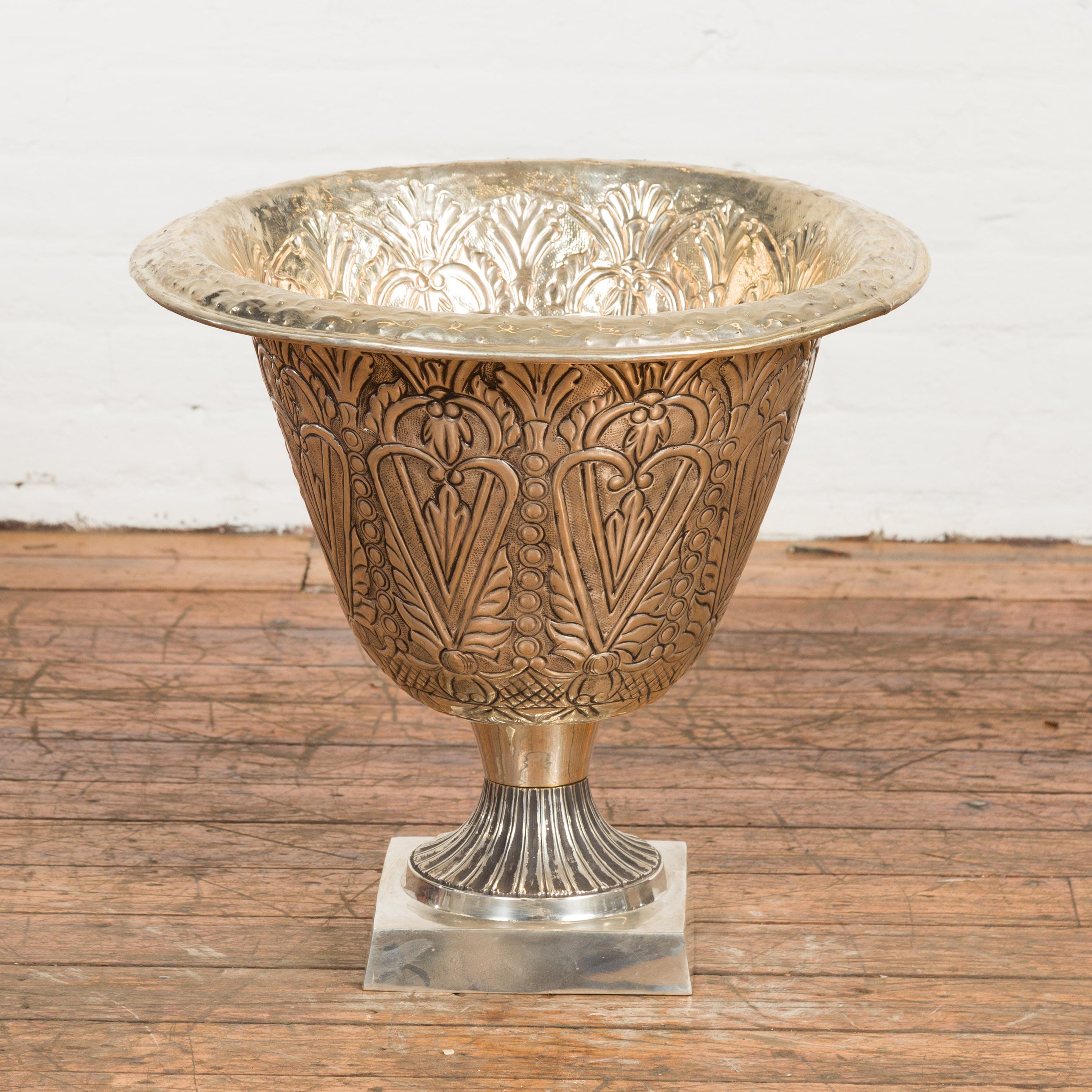 A vintage Indian silver over brass urn from the Mid-20th Century, with rich décor depicting stylized heart motifs and foliage on square base. Created in India during the Midcentury period, this silver over brass urn attracts our attention with its