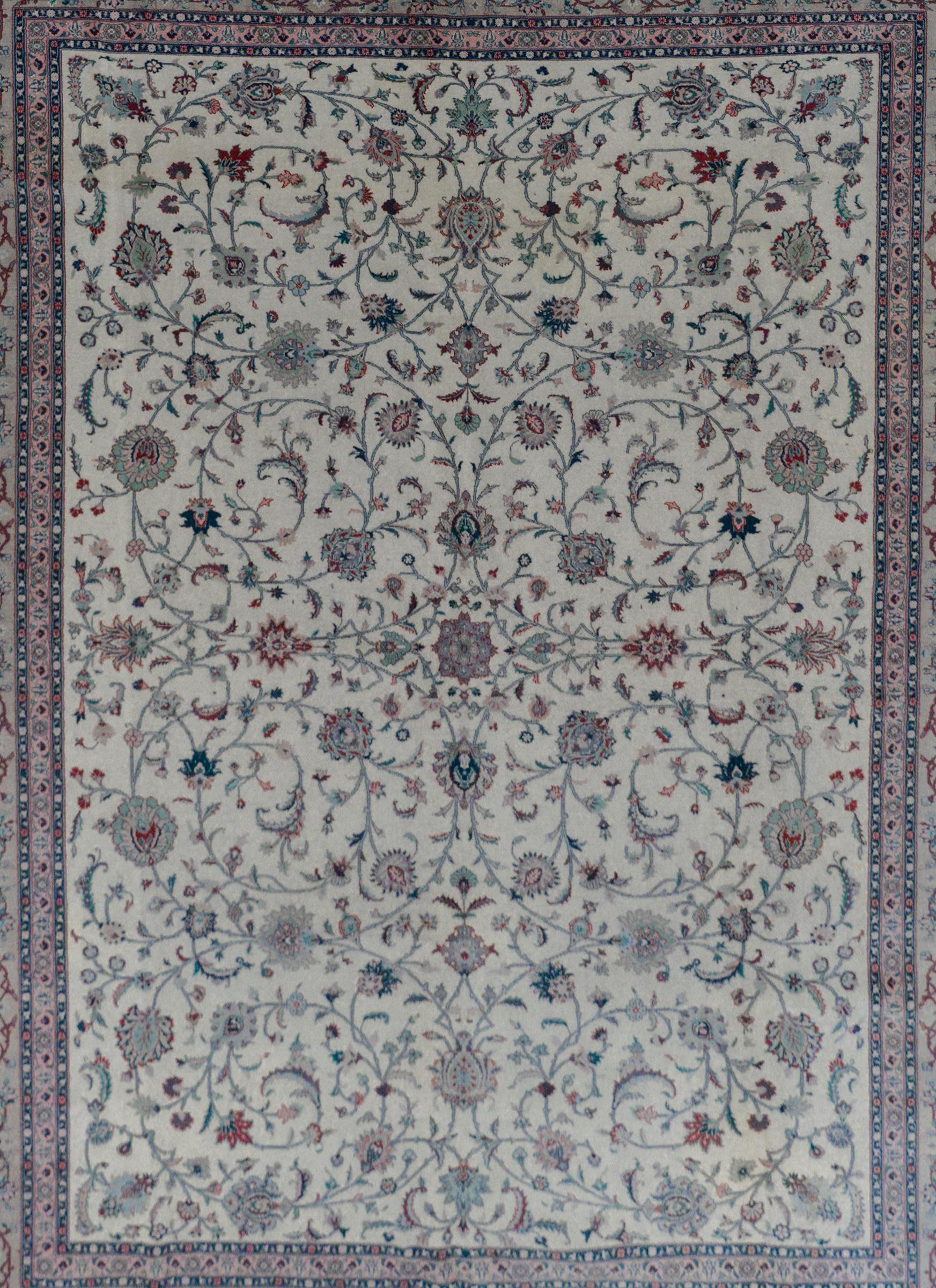A fantastic vintage Indian Tabriz rug with an all-over pattern of large-scale flowers and scrolling vines woven in crimson, light and dark indigo, teal and pink all on a cream colored background. The border is outstanding with a floral and scrolling