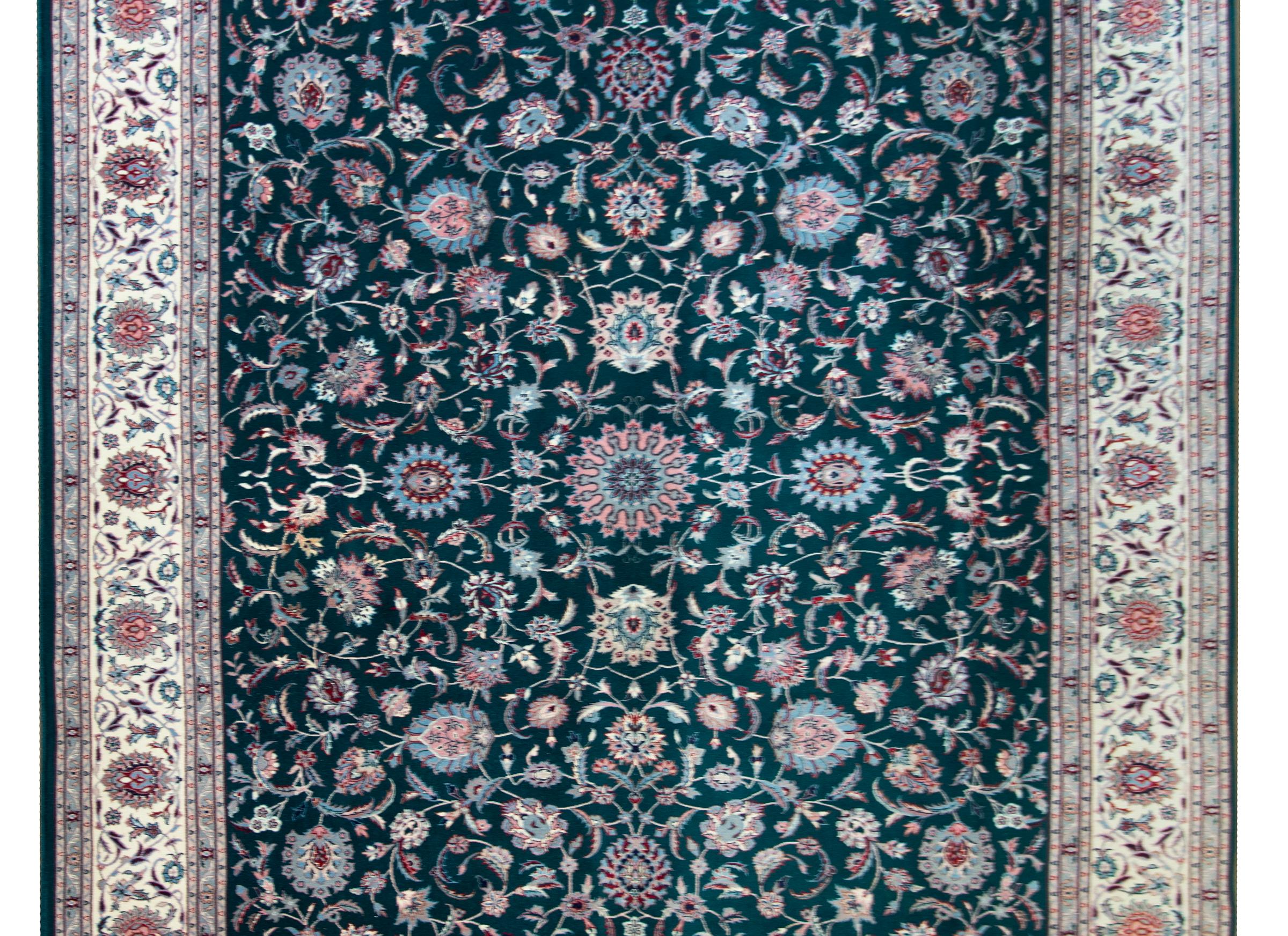 A wonderful late 20th century hand-knotted wool Indian rug with a Tabriz pattern containing an allover large-scale floral and scrolling vine pattern woven in light indigo, pink, crimson, and white, set against a dark indigo background, and