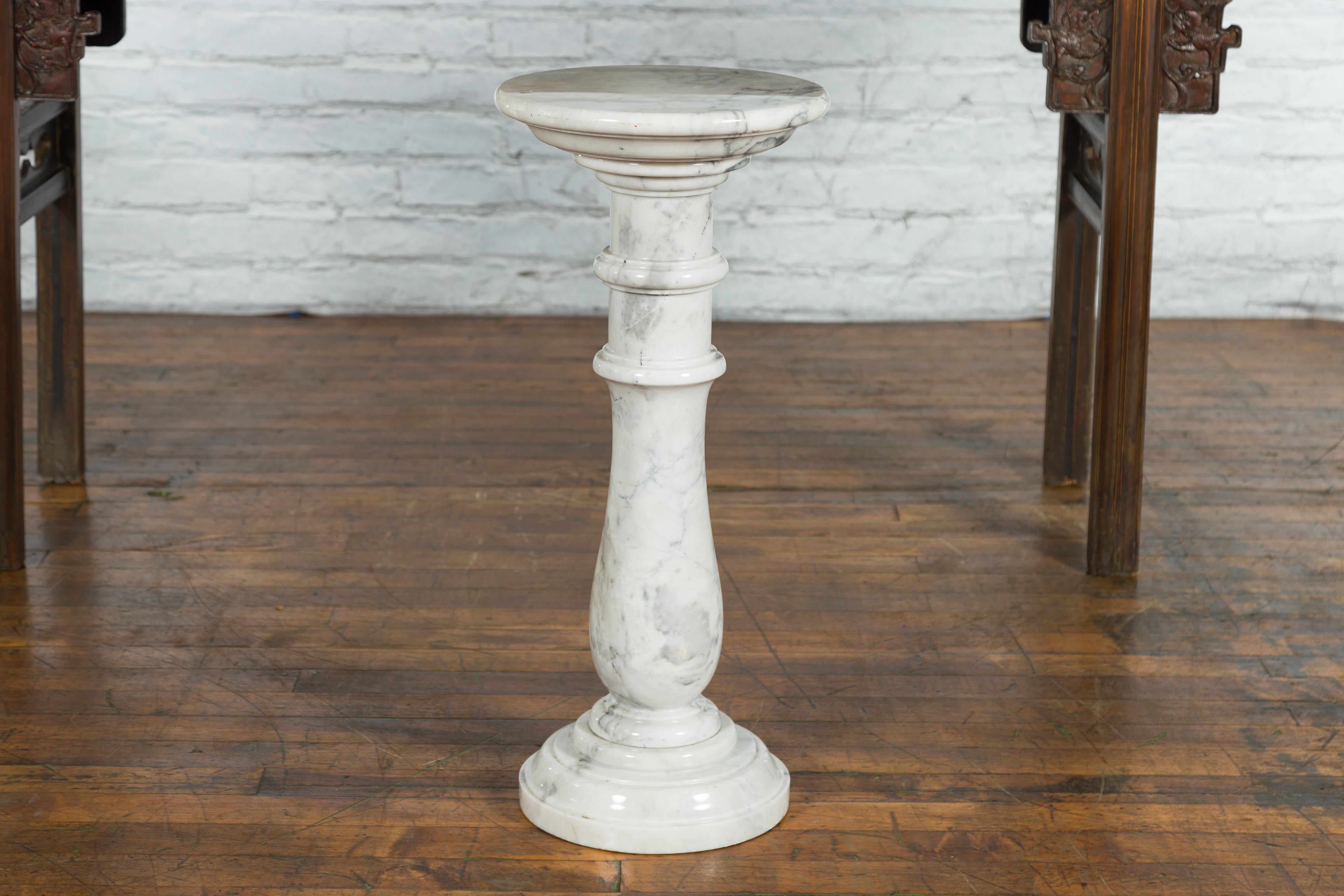 A vintage Indian white veined marble pedestal with baluster base and circular top. Created in India during the midcentury period, this marble pedestal will compliment any home decor beautifully. A circular top tapers down to rest on a