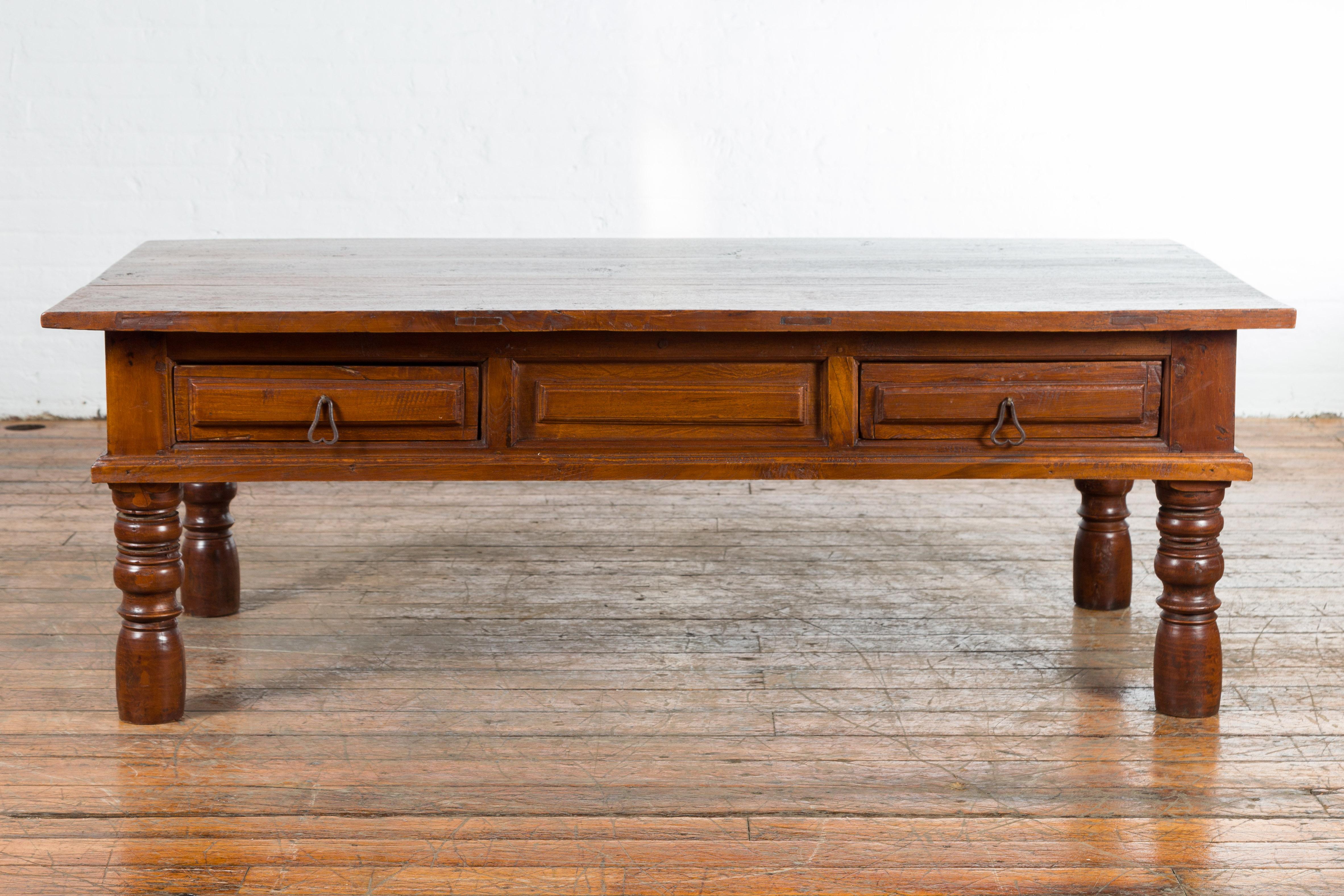 An Indian vintage coffee table from the mid 20th century, with two drawers and baluster legs. Created in India during the midcentury period, this coffee table features a rectangular planked top sitting above two drawers with raised panels and iron